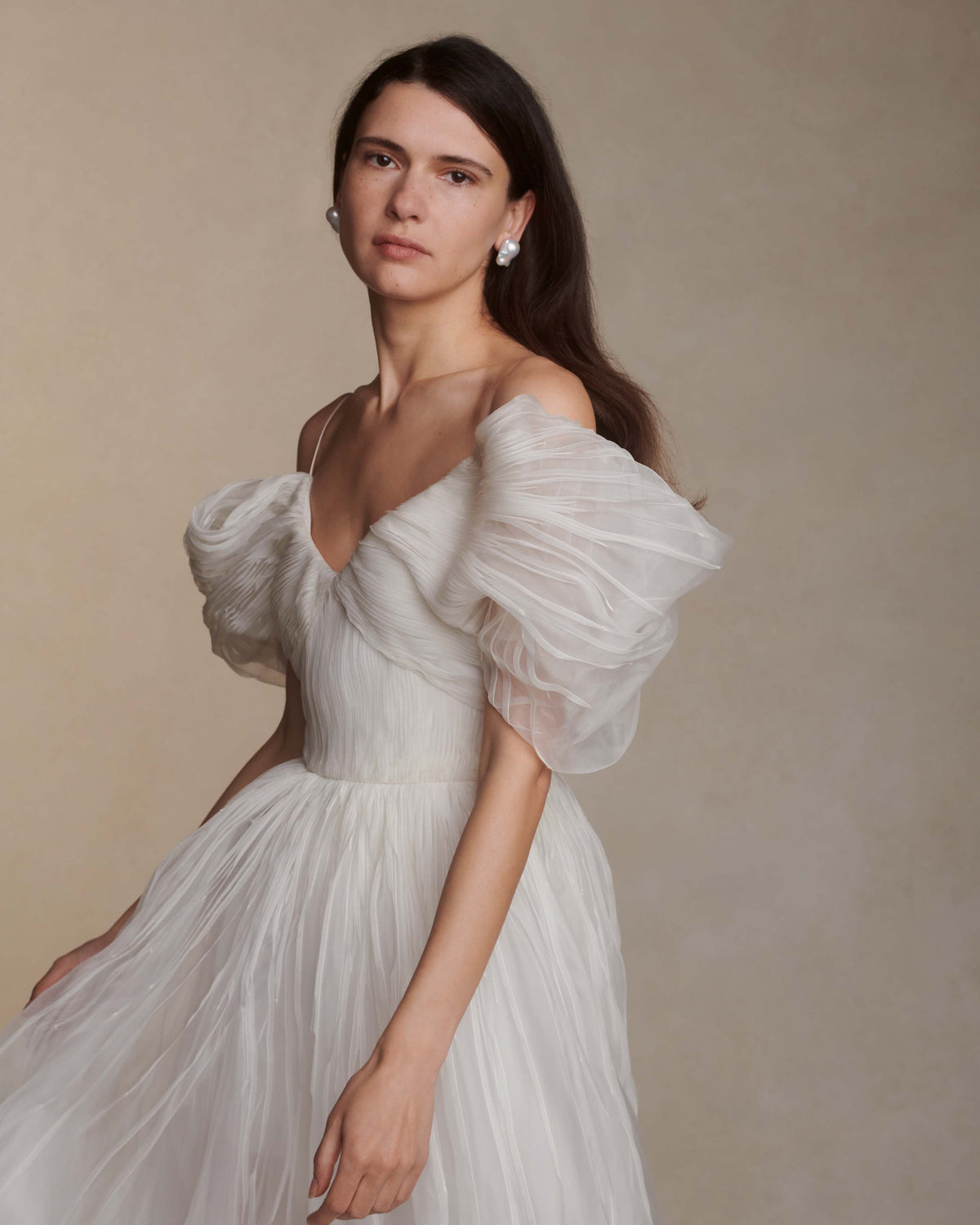 Hand tucked organza gown with spaghetti straps, V-neckline, and dramatic translucent ball skirt. Pin-tucked panels release from center front into swagged sleeve detail. Boned internal bustier, internal grosgrain waist belt, and center back zip closure.