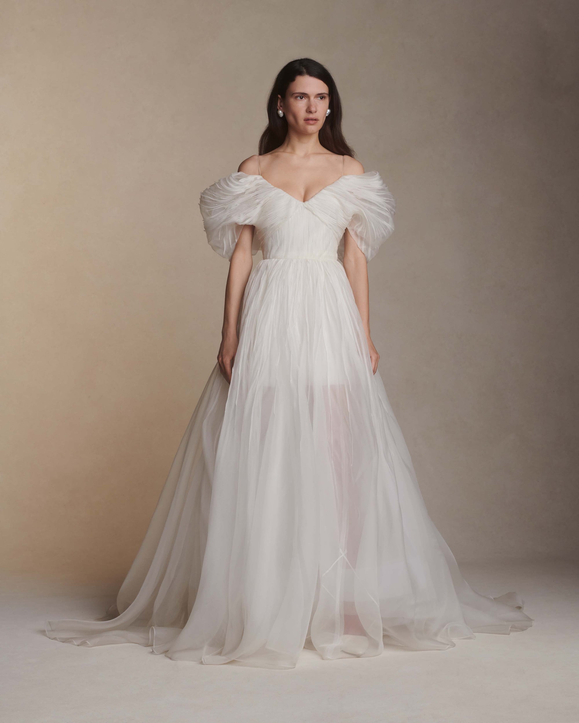 Hand tucked organza gown with spaghetti straps, V-neckline, and dramatic translucent ball skirt. Pin-tucked panels release from center front into swagged sleeve detail. Boned internal bustier, internal grosgrain waist belt, and center back zip closure.