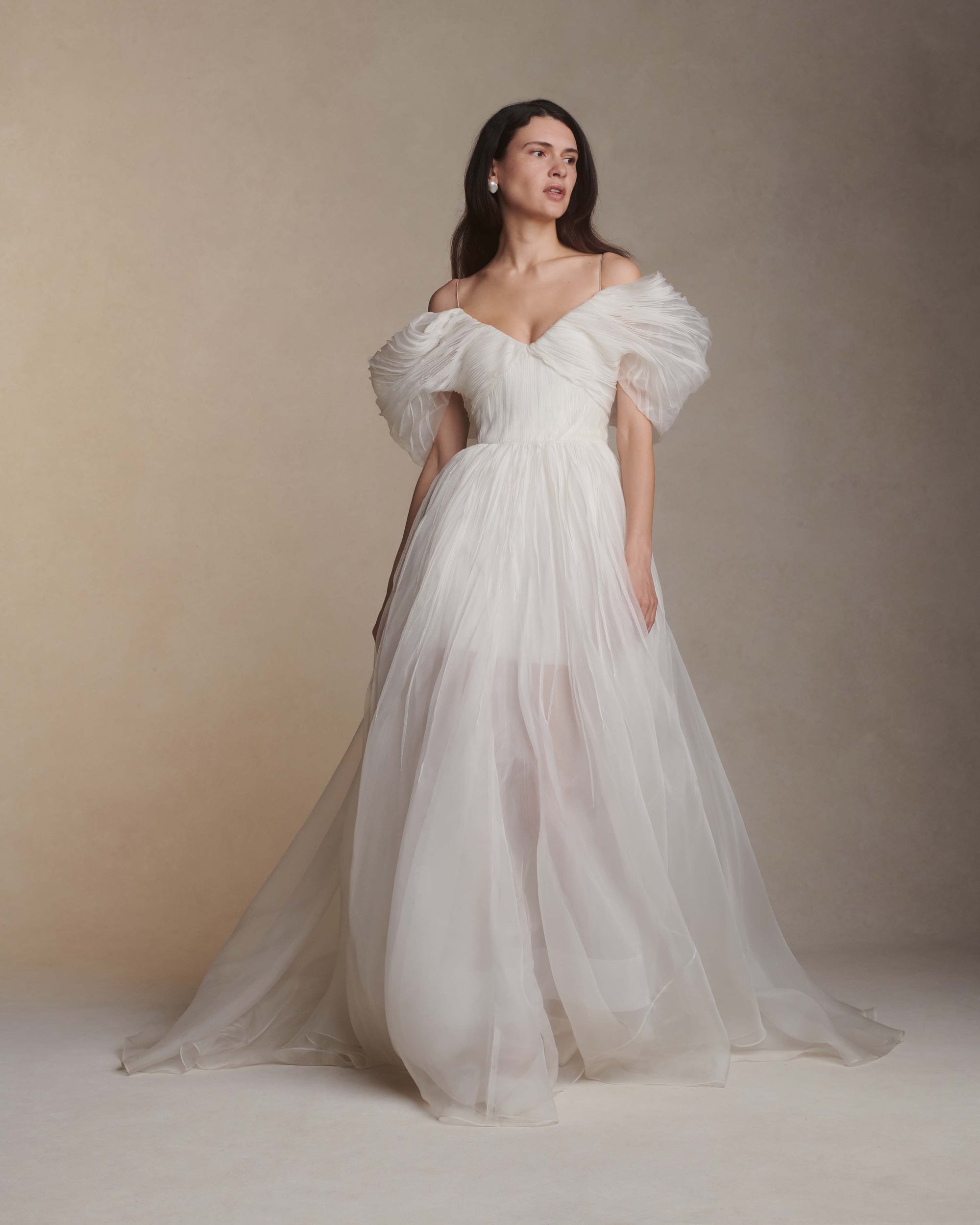 Hand tucked organza gown with spaghetti straps, V-neckline, and dramatic translucent ball skirt. Pin-tucked panels release from center front into swagged sleeve detail. Boned internal bustier, internal grosgrain waist belt, and center back zip closure.
