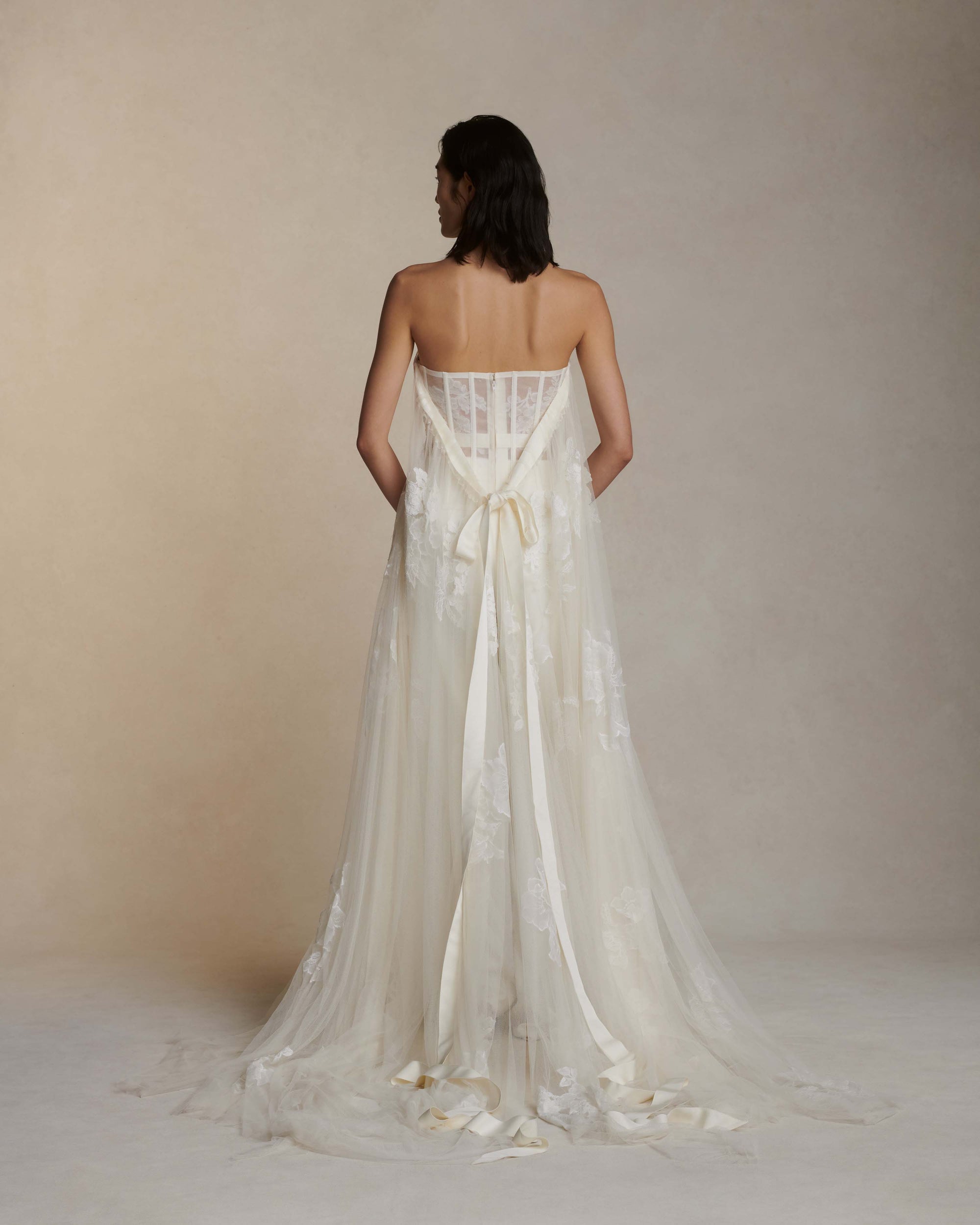 Soft tulle strapless corset top with sheer floral organza back. Hand appliquéd and draped through bodice and overflowing down side body. Tulle and lace train tunneled through grosgrain ribbon accent tie at back. Side boning and soft cups for support and center back zip to close.Styled with Miriam pant