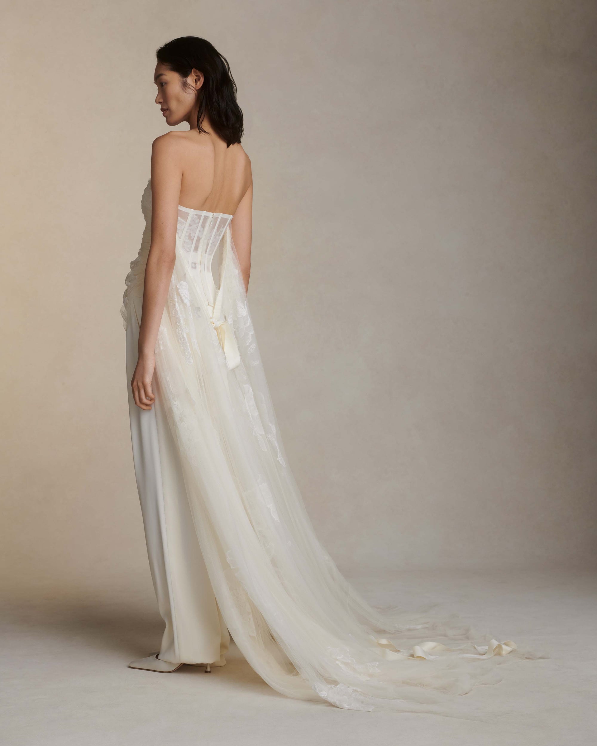 Soft tulle strapless corset top with sheer floral organza back. Hand appliquéd and draped through bodice and overflowing down side body. Tulle and lace train tunneled through grosgrain ribbon accent tie at back. Side boning and soft cups for support and center back zip to close.Styled with Miriam pant