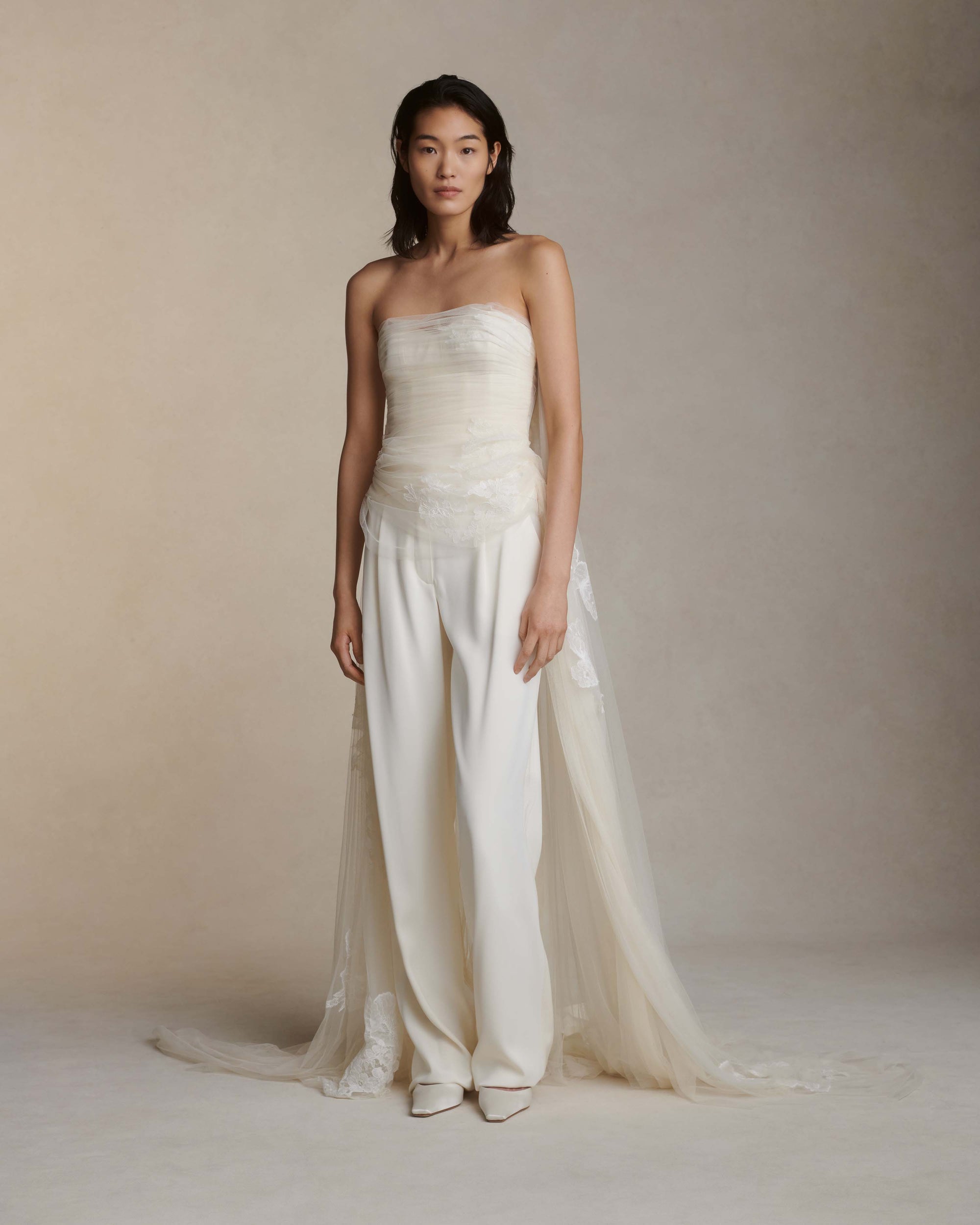 Soft tulle strapless corset top with sheer floral organza back. Hand appliquéd and draped through bodice and overflowing down side body. Tulle and lace train tunneled through grosgrain ribbon accent tie at back. Side boning and soft cups for support and center back zip to close.Styled with Miriam pant