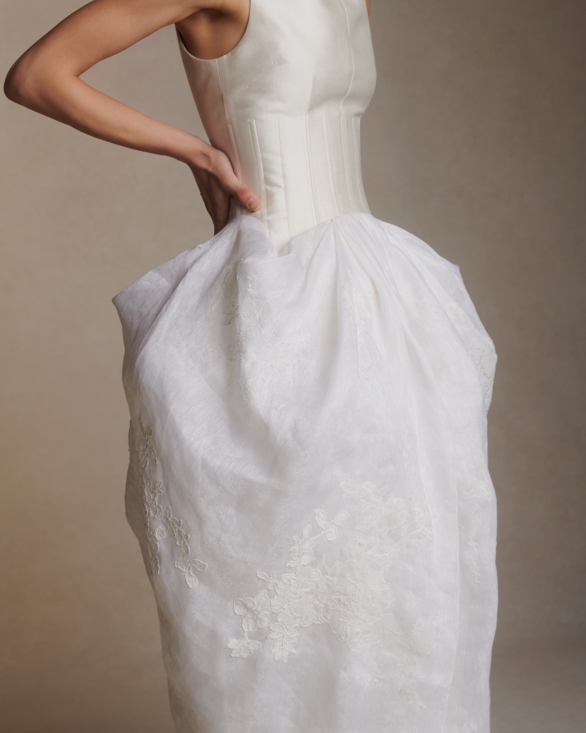 Silk wool twill and linen organza tea length gown. Structured boned bodice extends into dramatic sloped high neck that floats away from the body. Pleated and draped skirt is adorned with hand cut chantilly and corded lace appliques. Center back zip closure.