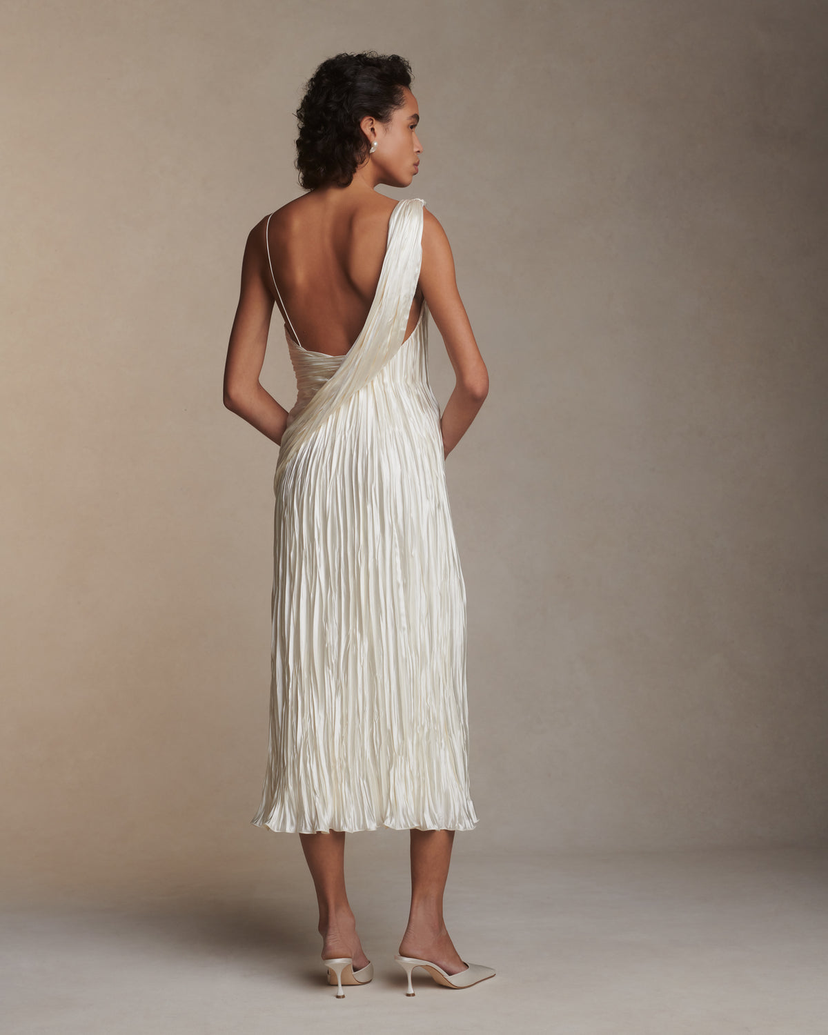 One shoulder pleated and hand crinkled silk wool cocktail length dress with dipped neckline. Asymmetric drape sweeps across front into a delicate twisted back detail. Boned internal bustier with soft cups, internal grosgrain waist belt and side zip closure.