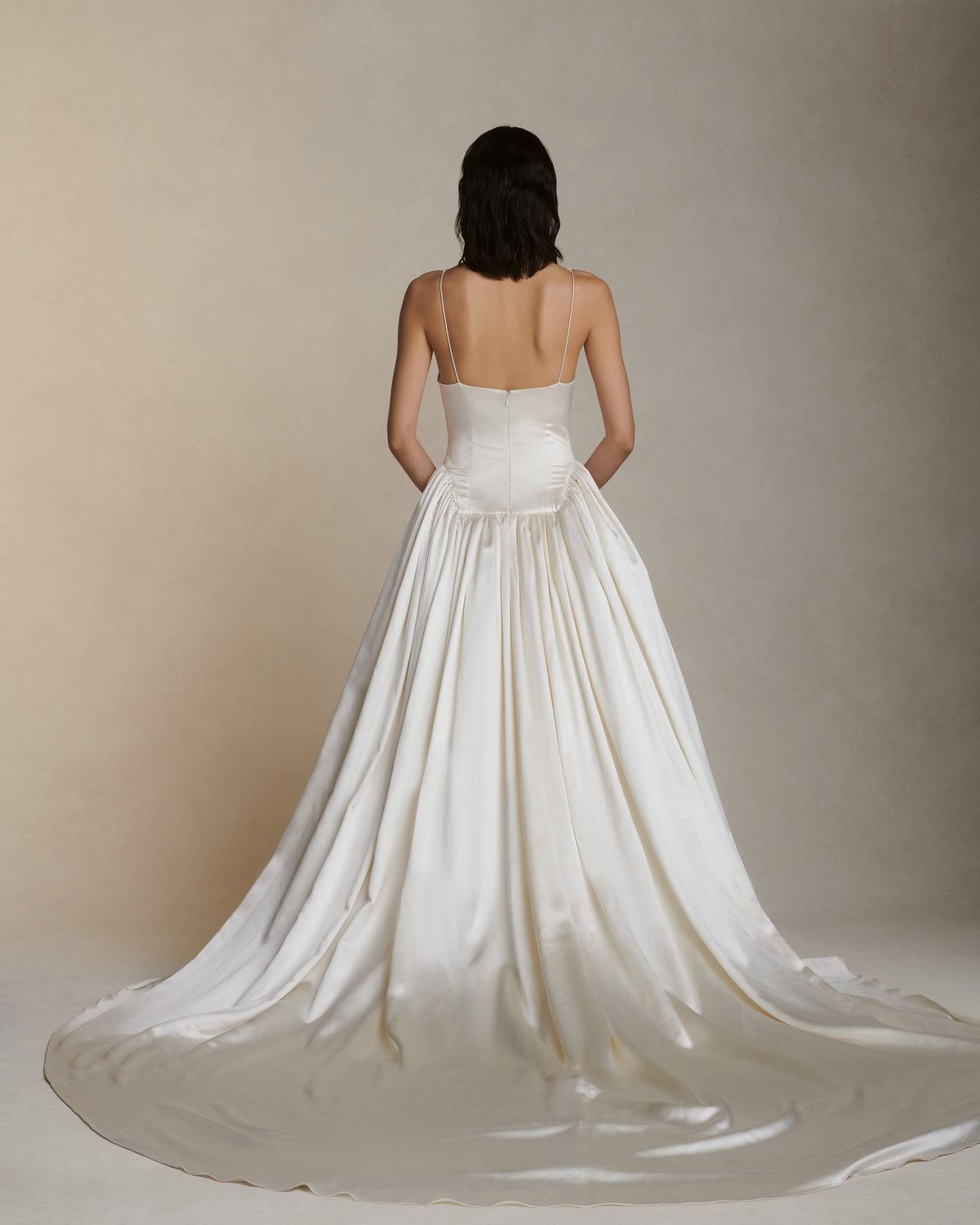 Deep V neck cathedral length gown with shirred, full skirt and elongated basque waist. Self lined, boned bodice for structure, and darts for shaping. Internal grosgrain waistband belt with three positions and center back zip. Fully lined soft skirt with exaggerated train, can can ruffle at hip for volume and structure.