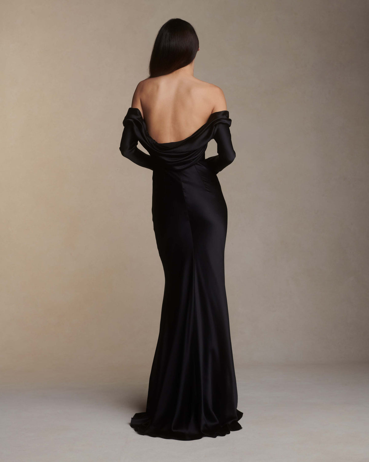 Wilted, long sleeve off the shoulder bias cut silk satin gown with criss-cross draping detail across low back. Darts at bust for shaping and 5 inch slit opening at inner wrist. Boned internal bustier with grosgrain, three closure position belt, wireless cups, and center back external zip. Fully lined skirt. Floor length.
