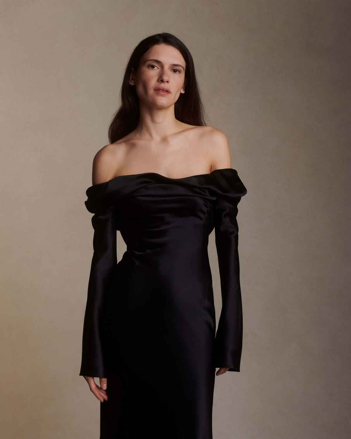 Wilted, long sleeve off the shoulder bias cut silk satin gown with criss-cross draping detail across low back. Darts at bust for shaping and 5 inch slit opening at inner wrist. Boned internal bustier with grosgrain, three closure position belt, wireless cups, and center back external zip. Fully lined skirt. Floor length.