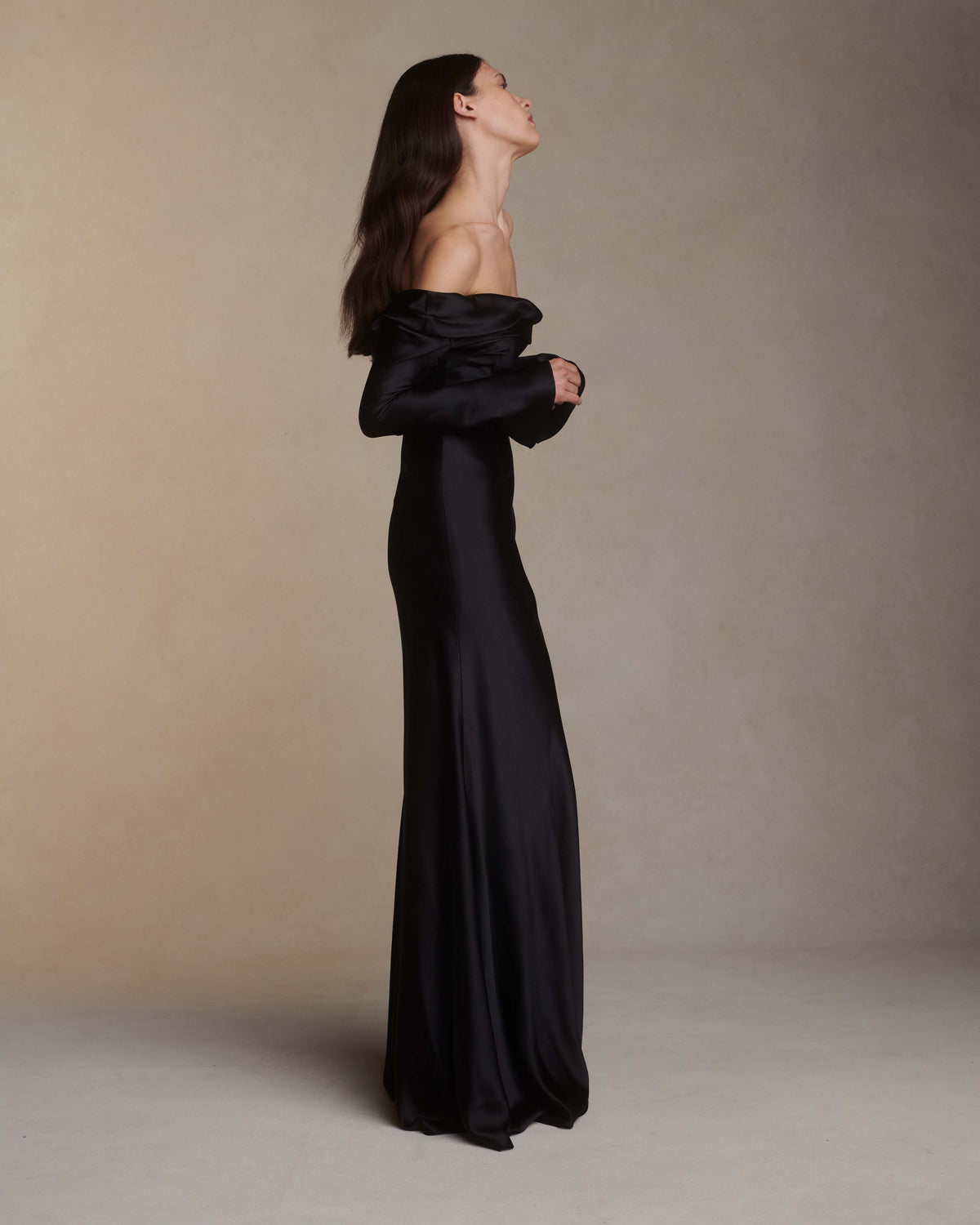 Wilted, long sleeve off the shoulder bias cut silk satin gown with criss-cross draping detail across low back. Darts at bust for shaping and 5 inch slit opening at inner wrist. Boned internal bustier with grosgrain, three closure position belt, wireless cups, and center back external zip. Fully lined skirt. Floor length.