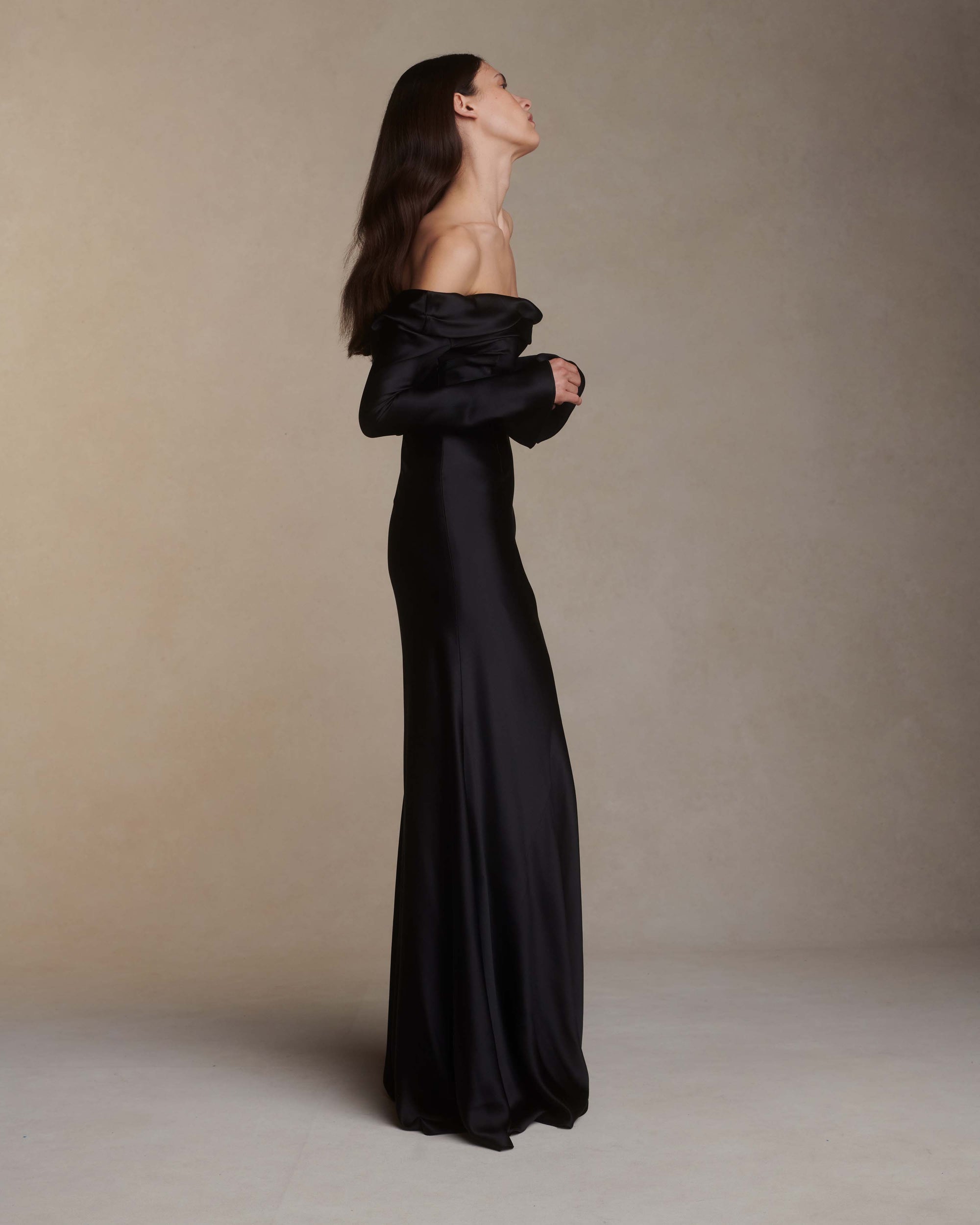 Wilted, long sleeve off the shoulder bias cut silk satin gown with criss-cross draping detail across low back. Darts at bust for shaping and 5 inch slit opening at inner wrist. Boned internal bustier with grosgrain, three closure position belt, wireless cups, and center back external zip. Fully lined skirt. Floor length.