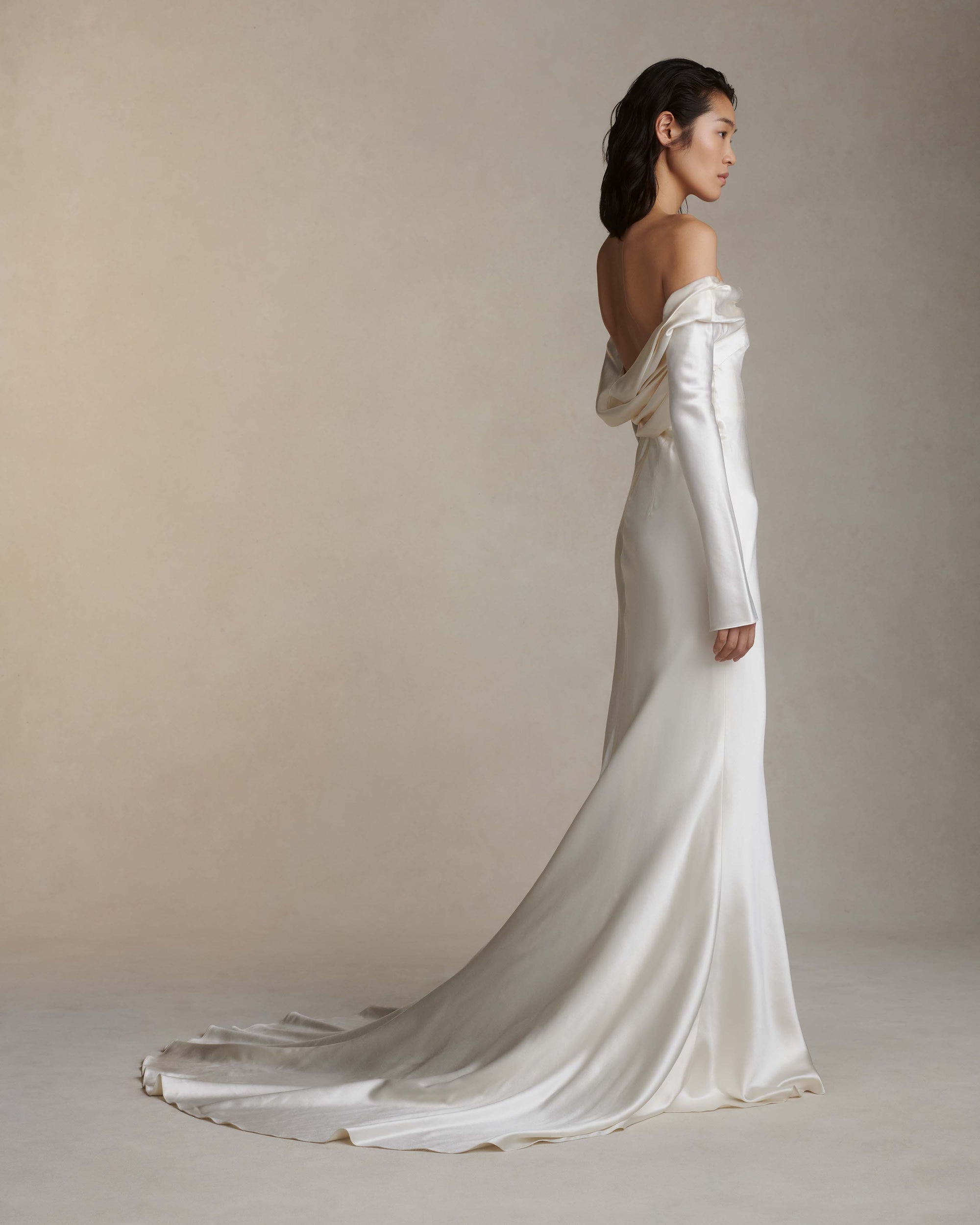 Wilted, long sleeve off the shoulder bias cut silk wool gown with criss-cross draping detail across low back. Darts at bust for shaping and 5 inch slit opening at inner wrist. Boned internal bustier with grosgrain, three closure position belt, wireless cups, and center back external zip. Fully lined skirt.