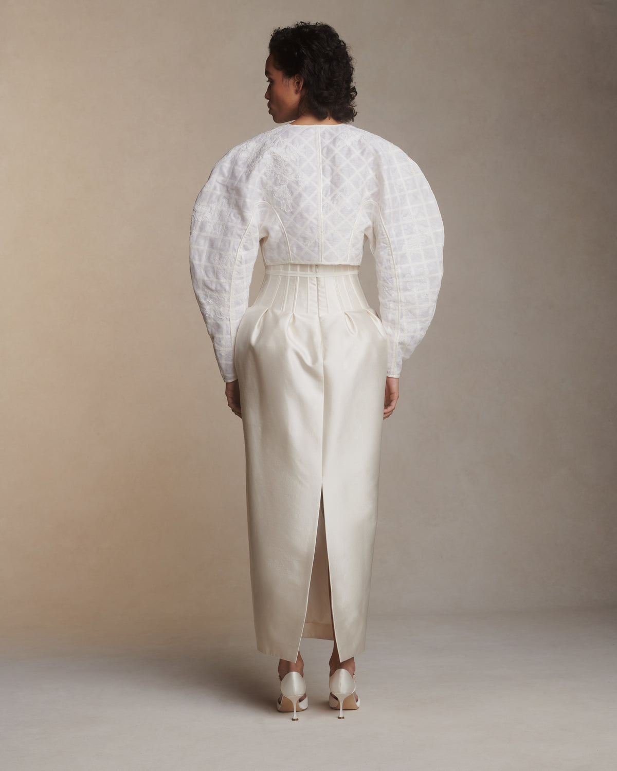 Sculptural linen organza cropped jacket framed with silk organza and grosgrain ribbon trellis detail. Hand cut and chantilly lace appliqued throughout. Satin piping detail and long grosgrain ribbon tie detail at center front. Covered button and loop closure at sleeve opening.Styled with Audra gown