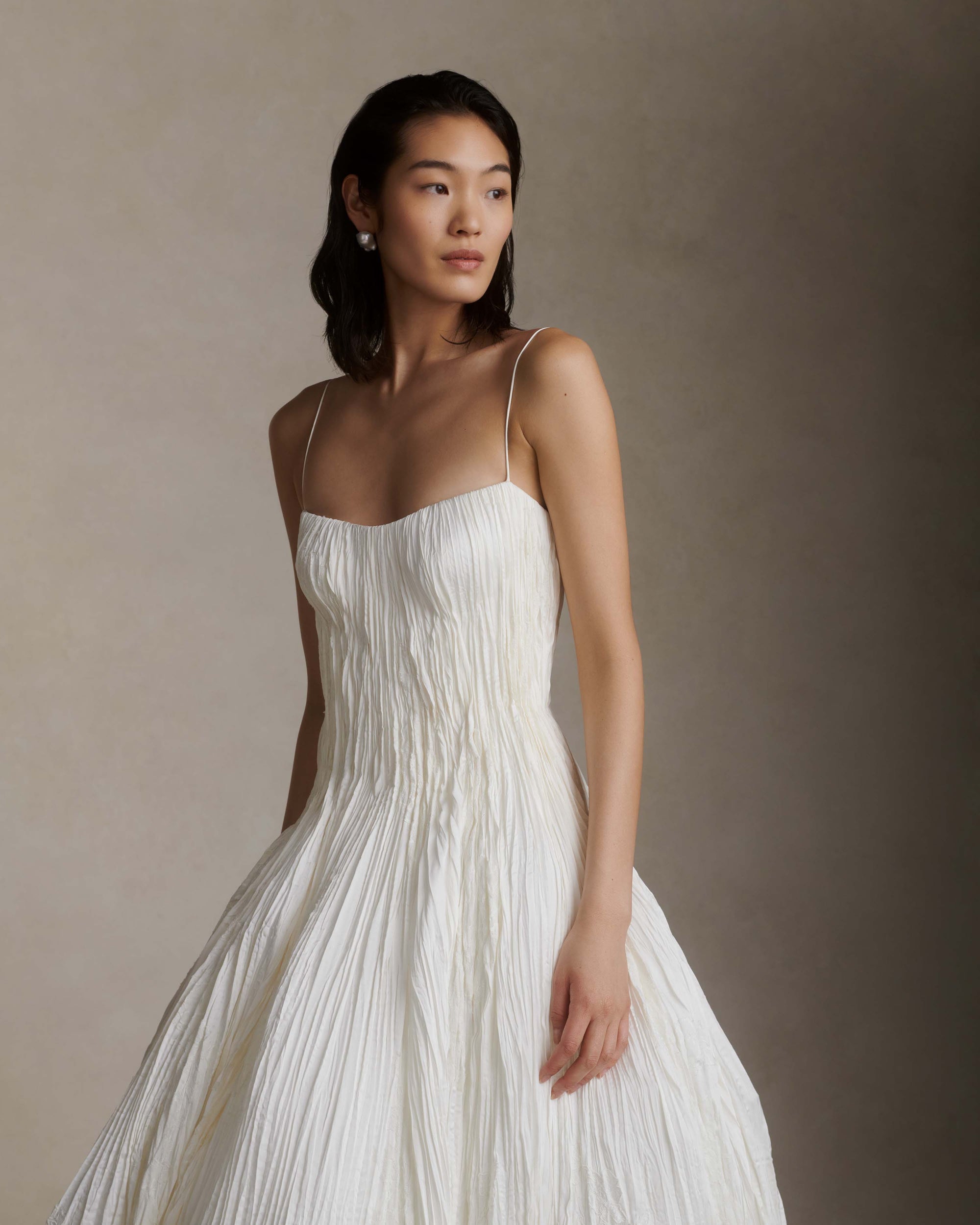 Hand crinkled and sunburst pleated satin gown with delicate spaghetti straps, dipped neckline, and dramatic bubbled skirt and train. Soft internal cups, boning, internal waist belt, invisible center back zip.