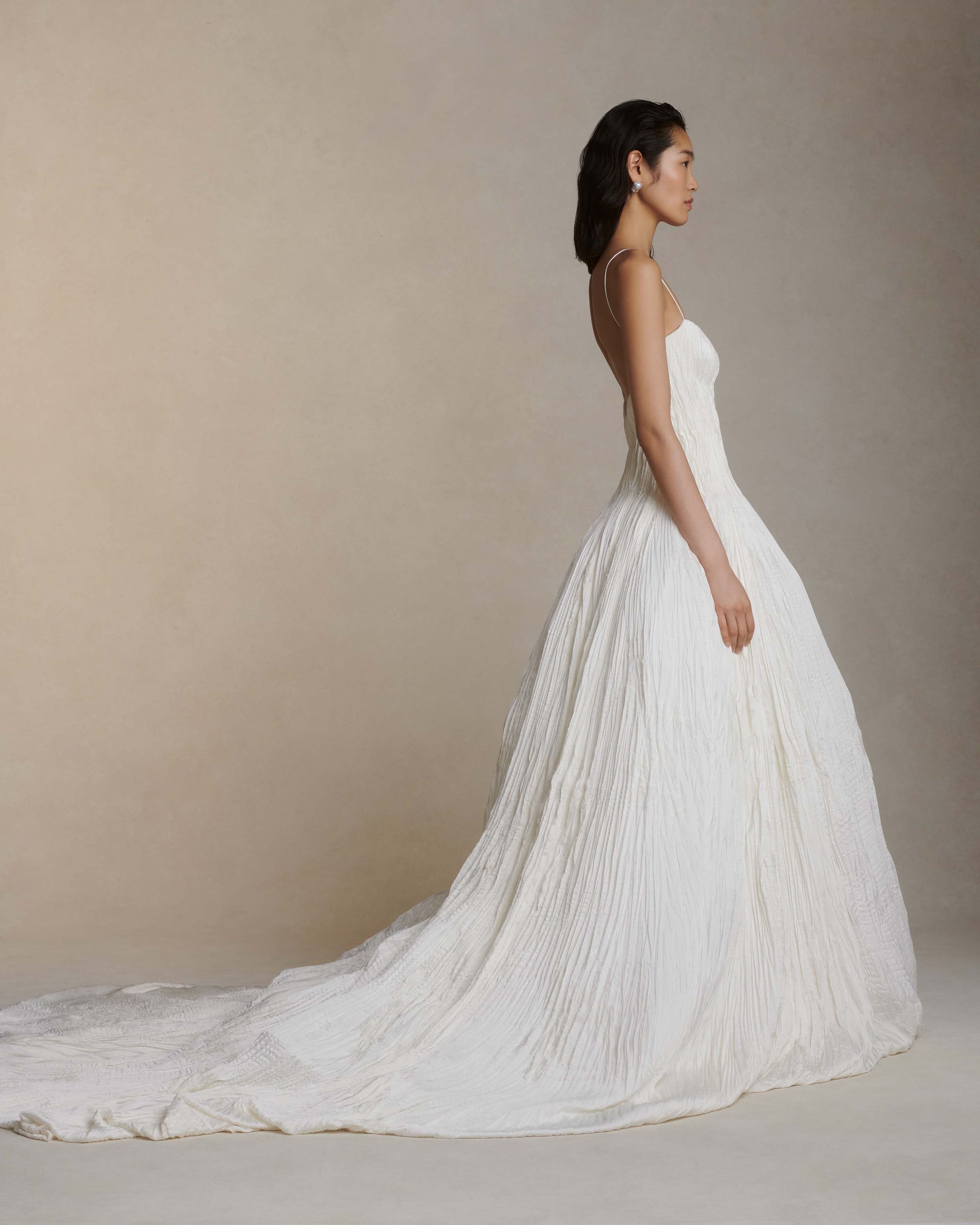 Hand crinkled and sunburst pleated satin gown with delicate spaghetti straps, dipped neckline, and dramatic bubbled skirt and train. Soft internal cups, boning, internal waist belt, invisible center back zip.