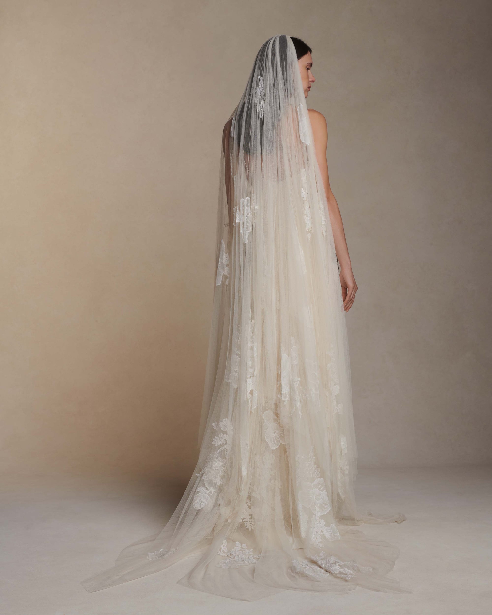 Pleated soft tulle veil decorated with hand cut Chantilly and corded lace appliqués throughout Undulating hem measures 85” at longest point.