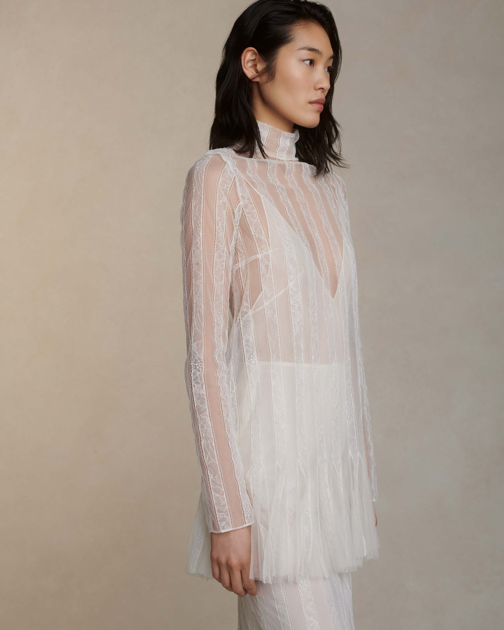 Long sleeve picot lace mini dress with hand appliqued floral chantilly lace stripes and soft tulle godets at hem. Foldover high neck with purl edge stitch detail. Nude slip lining, covered button and loop closure at center back neck.Styled with Henri