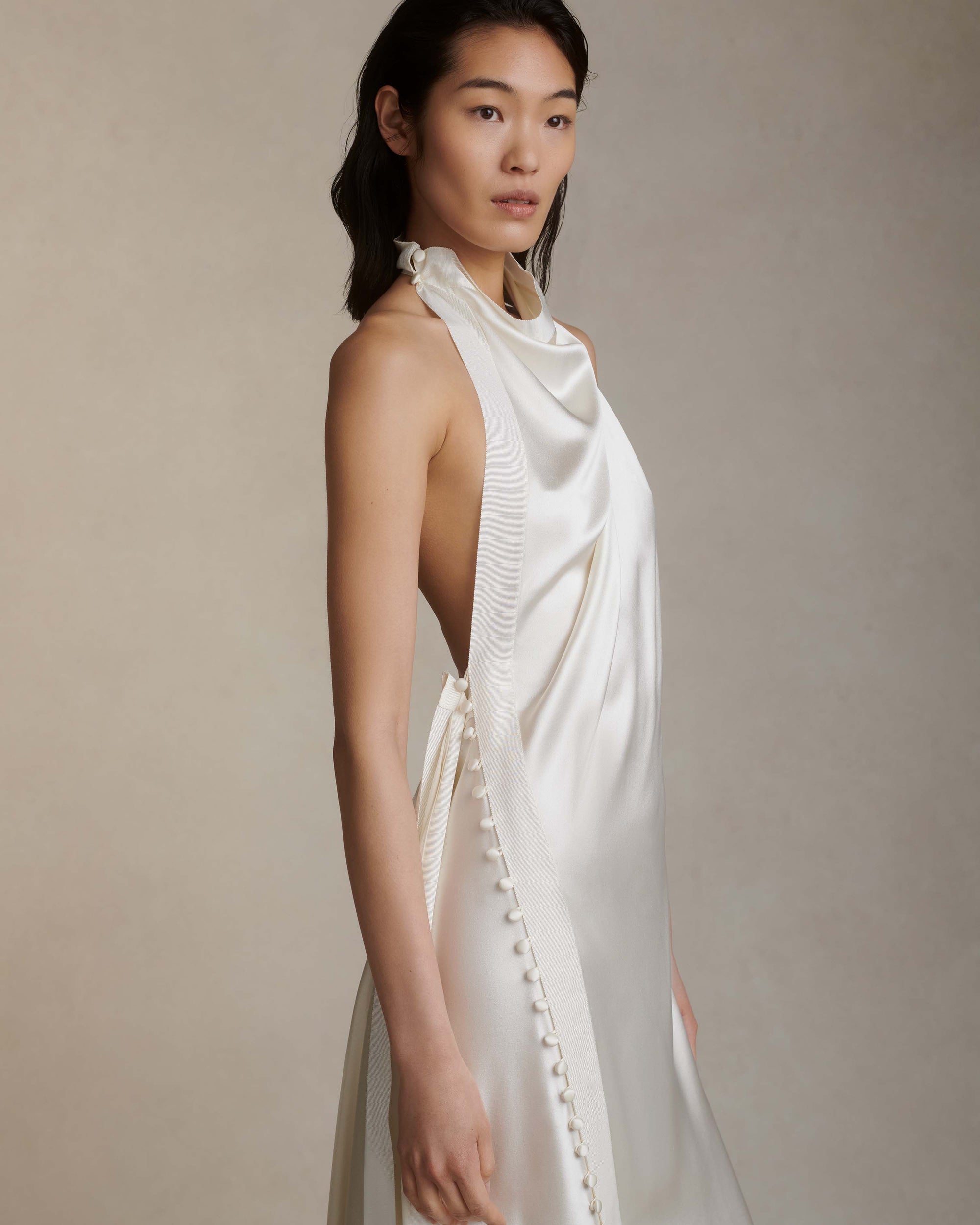 Silk crepe back satin handkerchief gown. Grosgrain edging and covered button detailing along side hip. Optional bustle loop on handkerchief corner hem. Slip on styling with button close at neck.
