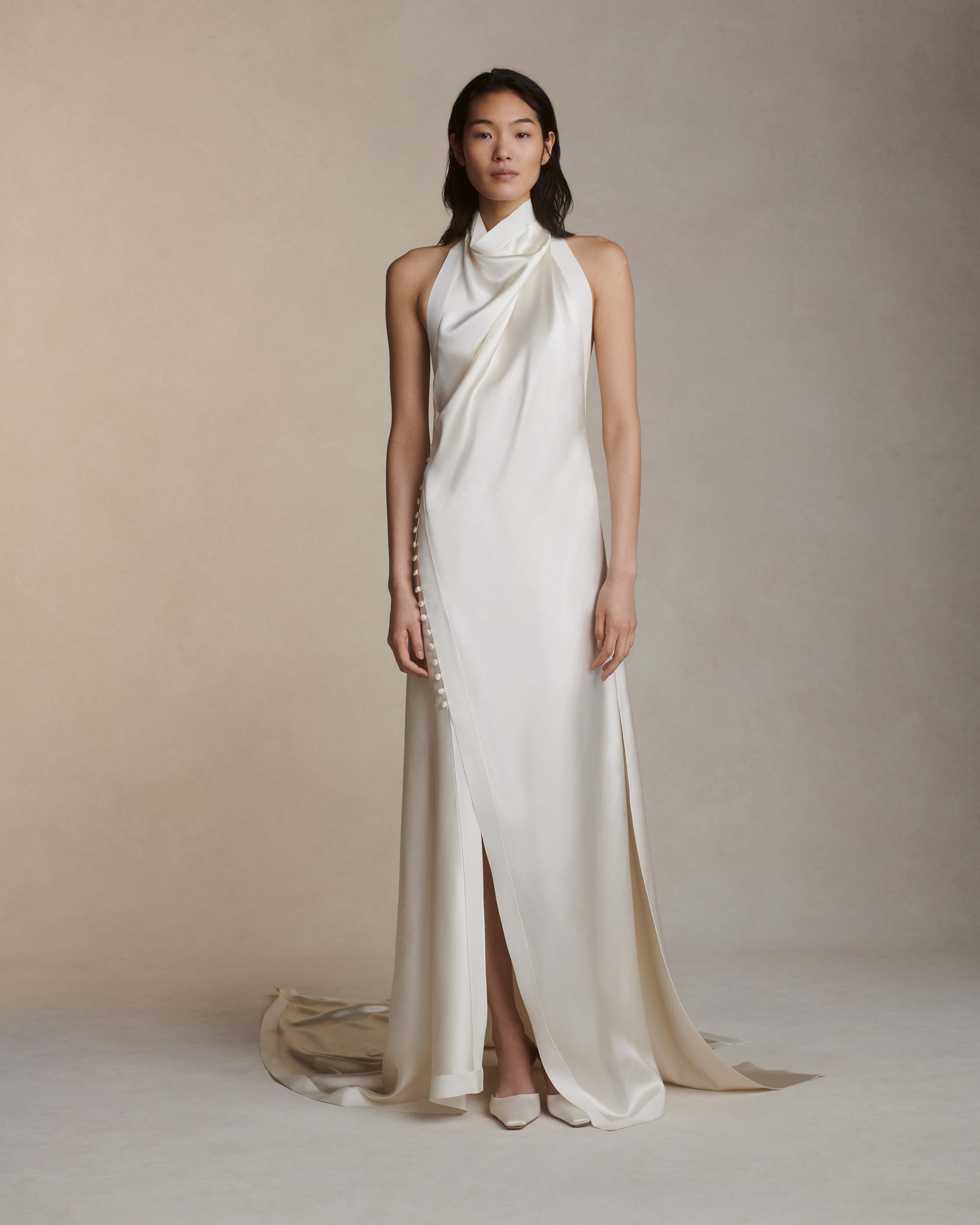 Silk crepe back satin handkerchief gown. Grosgrain edging and covered button detailing along side hip. Optional bustle loop on handkerchief corner hem. Slip on styling with button close at neck.