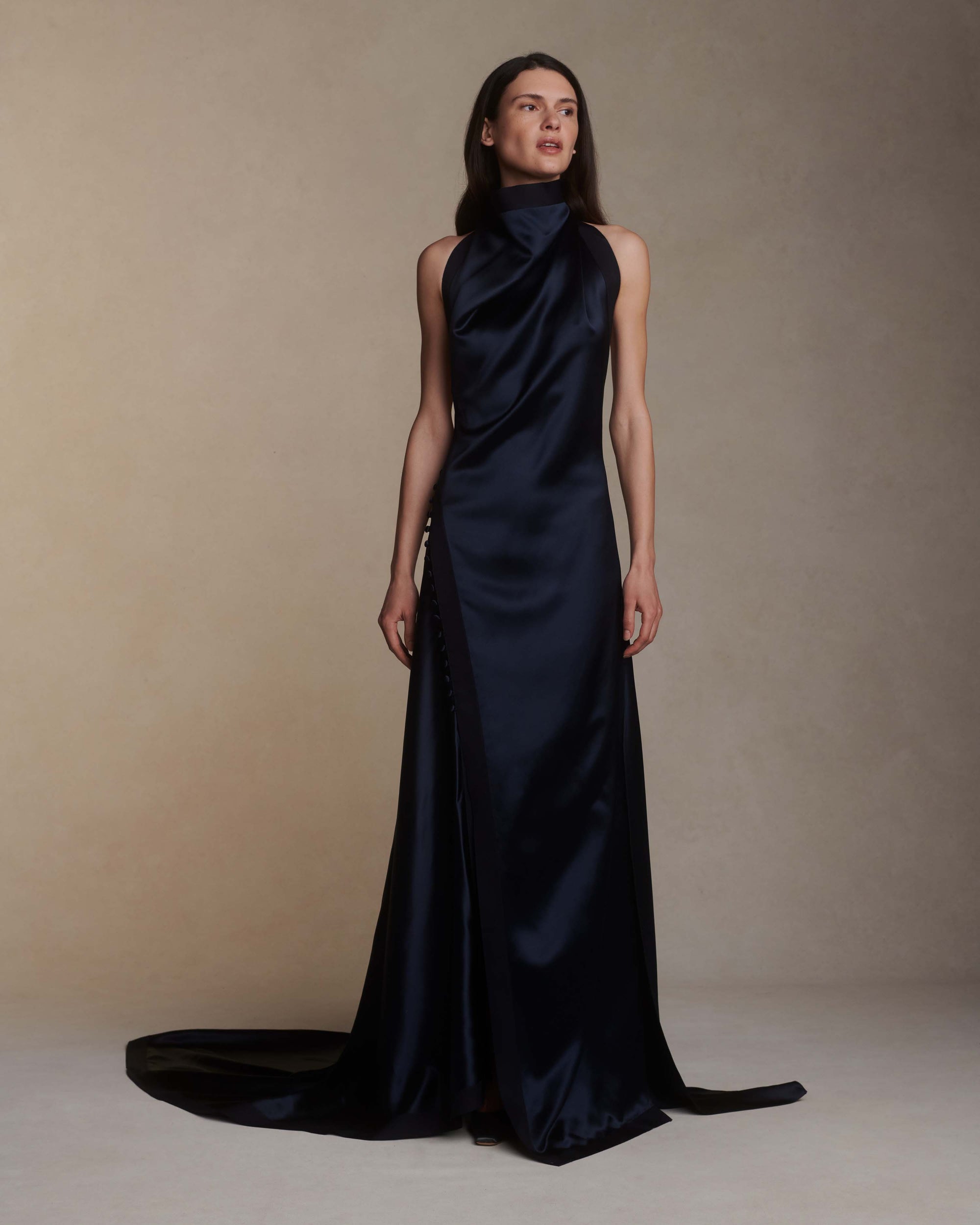 Silk crepe back satin handkerchief gown. Grosgrain edging and covered button detailing along side hip. Optional bustle loop on handkerchief corner hem. Slip on styling with button close at neck.