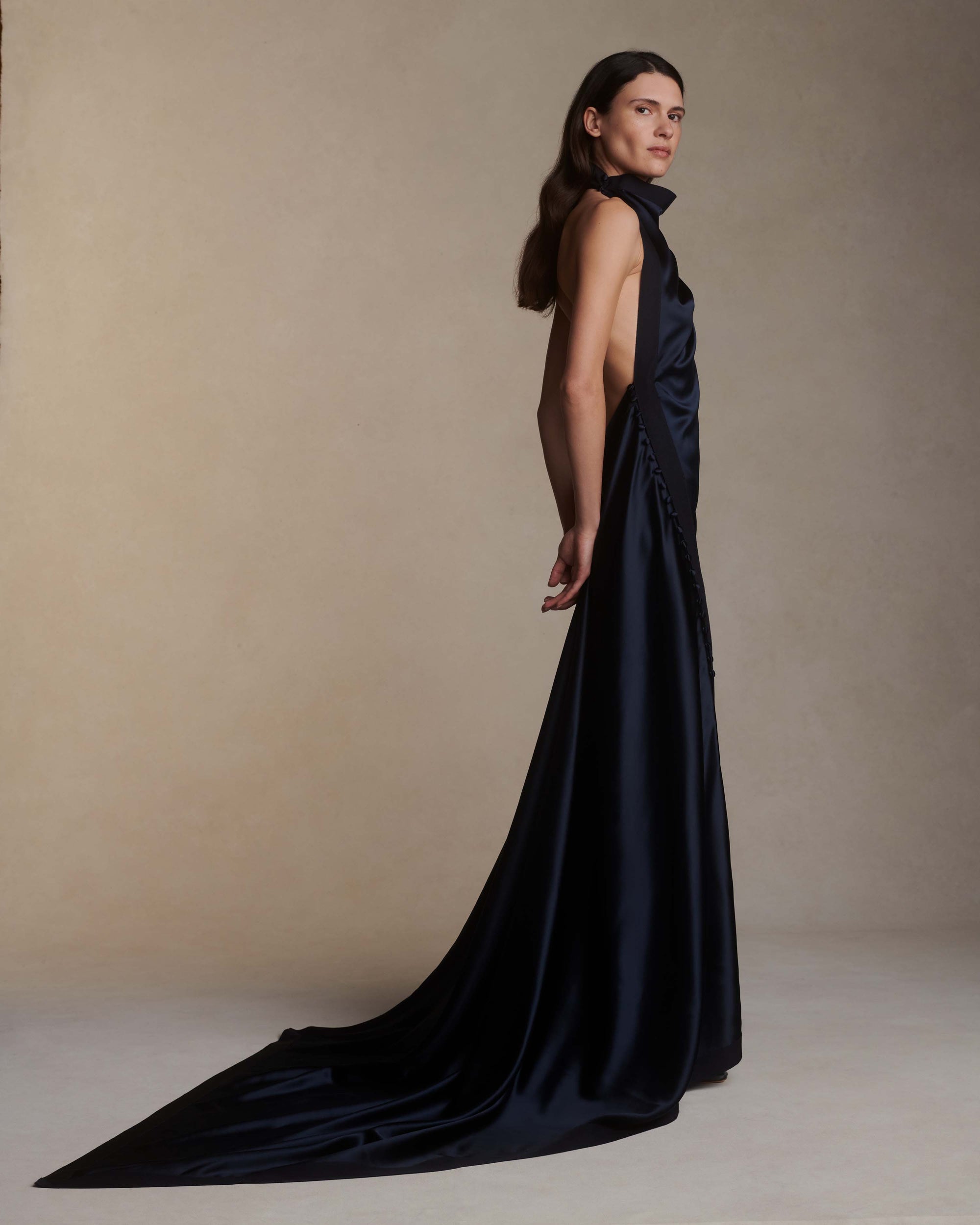 Silk crepe back satin handkerchief gown. Grosgrain edging and covered button detailing along side hip. Optional bustle loop on handkerchief corner hem. Slip on styling with button close at neck.