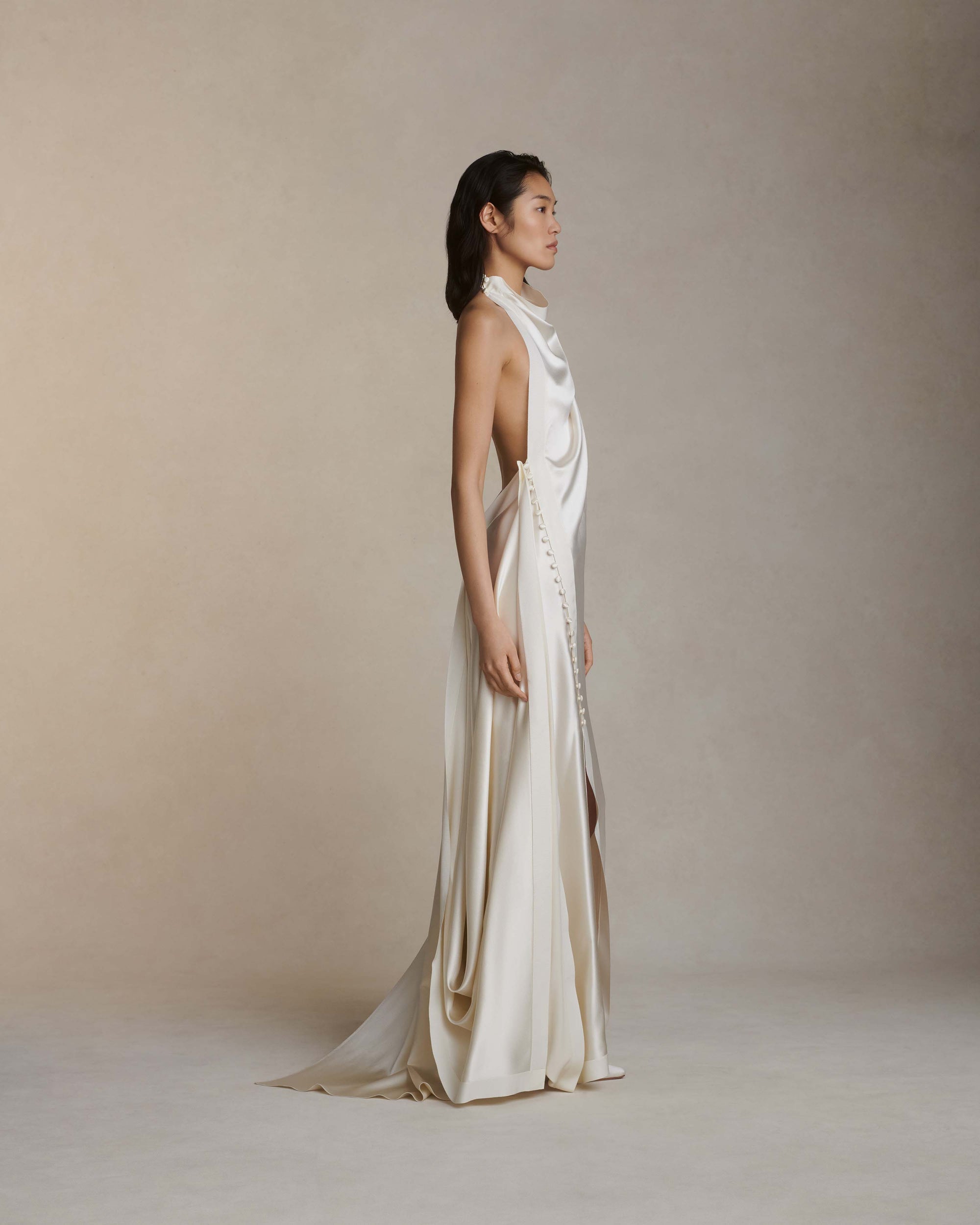 Silk crepe back satin handkerchief gown. Grosgrain edging and covered button detailing along side hip. Optional bustle loop on handkerchief corner hem. Slip on styling with button close at neck.