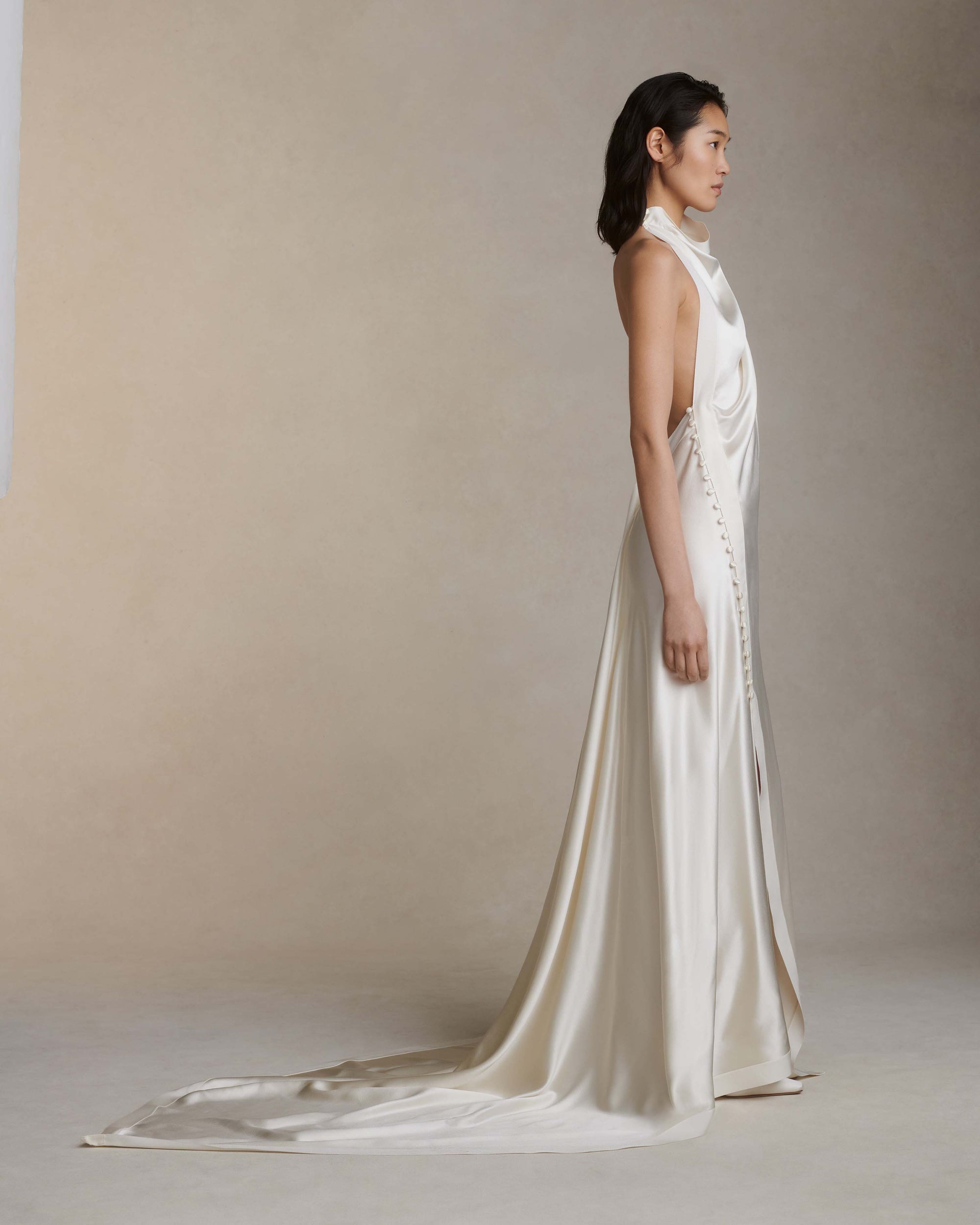 Silk crepe back satin handkerchief gown. Grosgrain edging and covered button detailing along side hip. Optional bustle loop on handkerchief corner hem. Slip on styling with button close at neck.