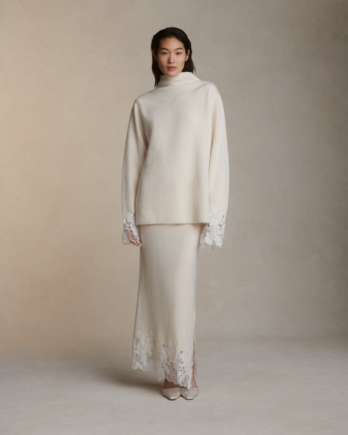 Silk cashmere knit pullover with hand cut chantilly and corded lace applique at sleeve opening. Angled high neck with rib knit sloped shoulder yoke. Side slits at sleeve opening. Rib knit hem.Styled with Viv skirt