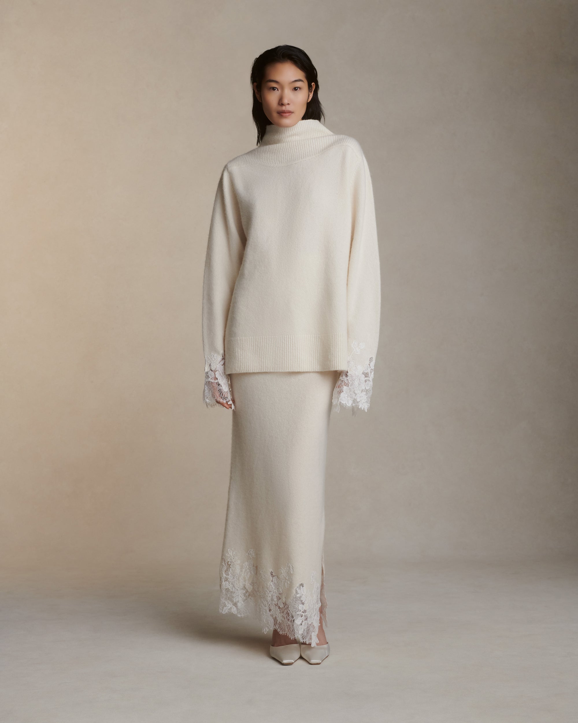 Silk cashmere knit pullover with hand cut chantilly and corded lace applique at sleeve opening. Angled high neck with rib knit sloped shoulder yoke. Side slits at sleeve opening. Rib knit hem.Styled with Viv skirt