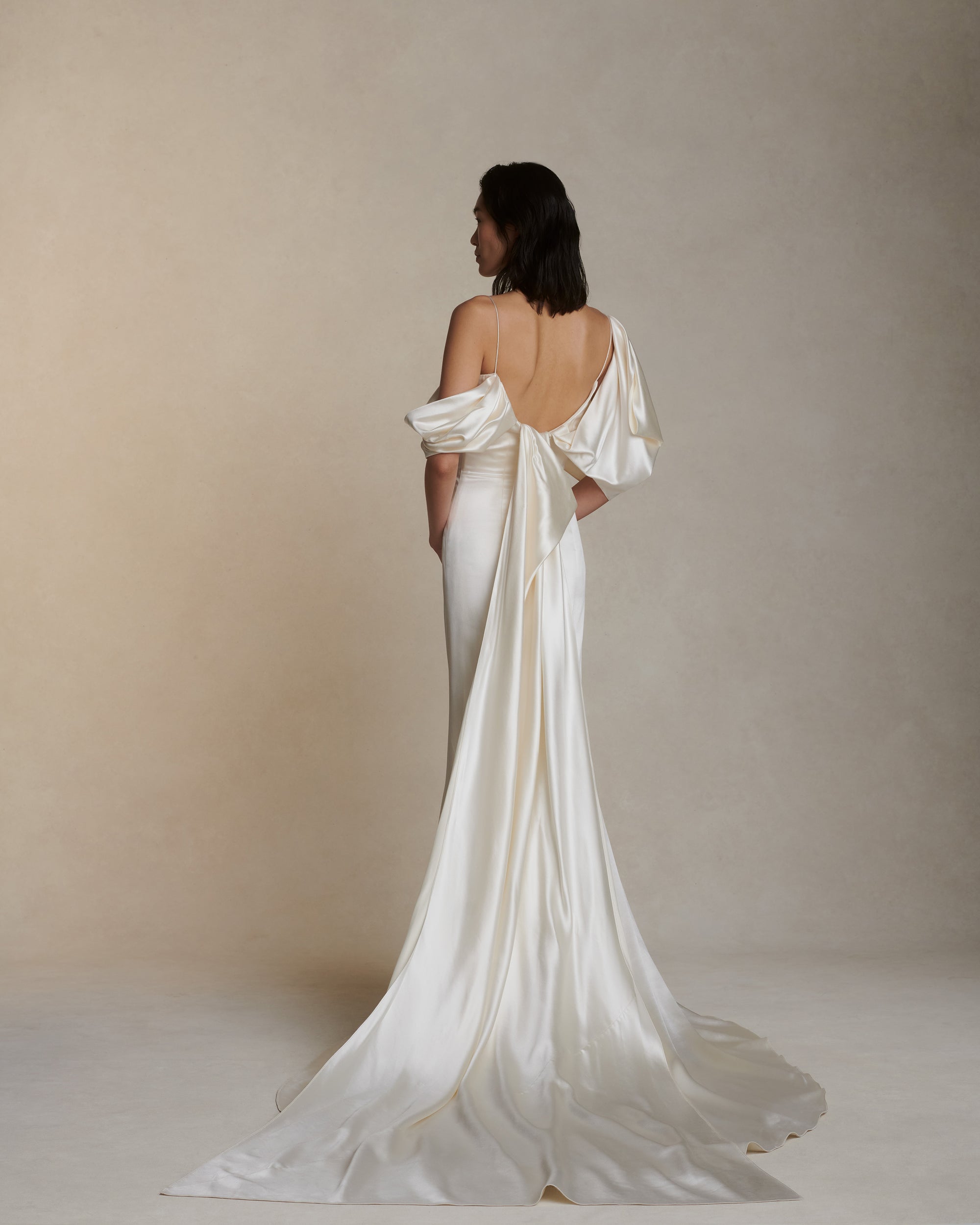 Silk wool gown with asymmetrical swagged sleeve. Detachable watteau train pouring down center back. External darts for shaping and spaghetti straps for contrast. Soft internal bustier with side boning, cups, and grosgrain belt with 3 hook position. Low center back zip, hook and eye closure.