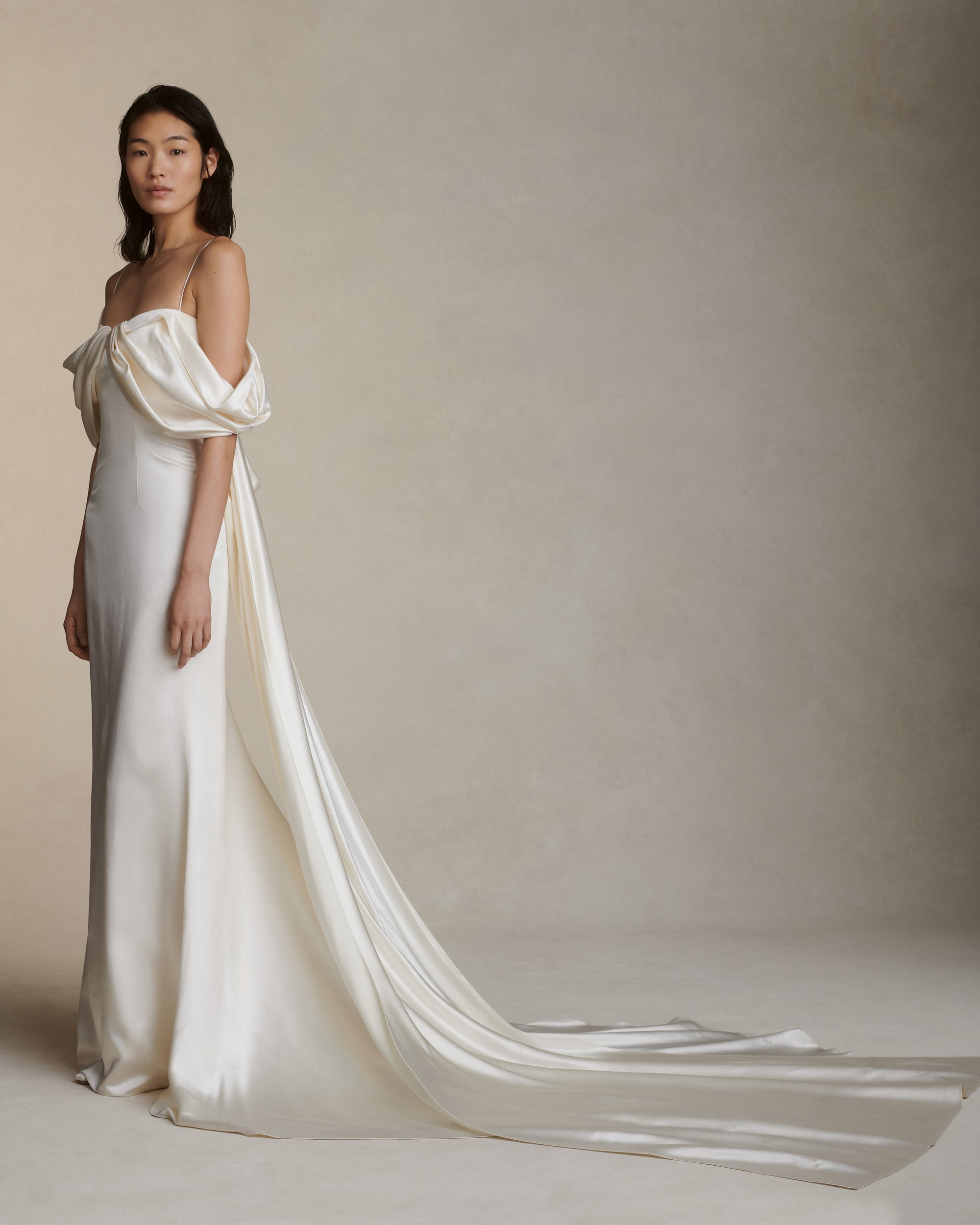 Silk wool gown with asymmetrical swagged sleeve. Detachable watteau train pouring down center back. External darts for shaping and spaghetti straps for contrast. Soft internal bustier with side boning, cups, and grosgrain belt with 3 hook position. Low center back zip, hook and eye closure.