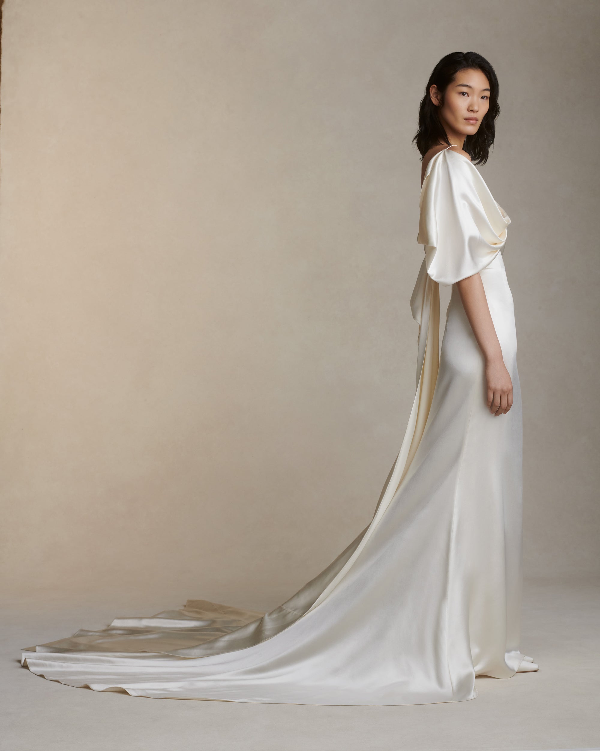 Silk wool gown with asymmetrical swagged sleeve. Detachable watteau train pouring down center back. External darts for shaping and spaghetti straps for contrast. Soft internal bustier with side boning, cups, and grosgrain belt with 3 hook position. Low center back zip, hook and eye closure.