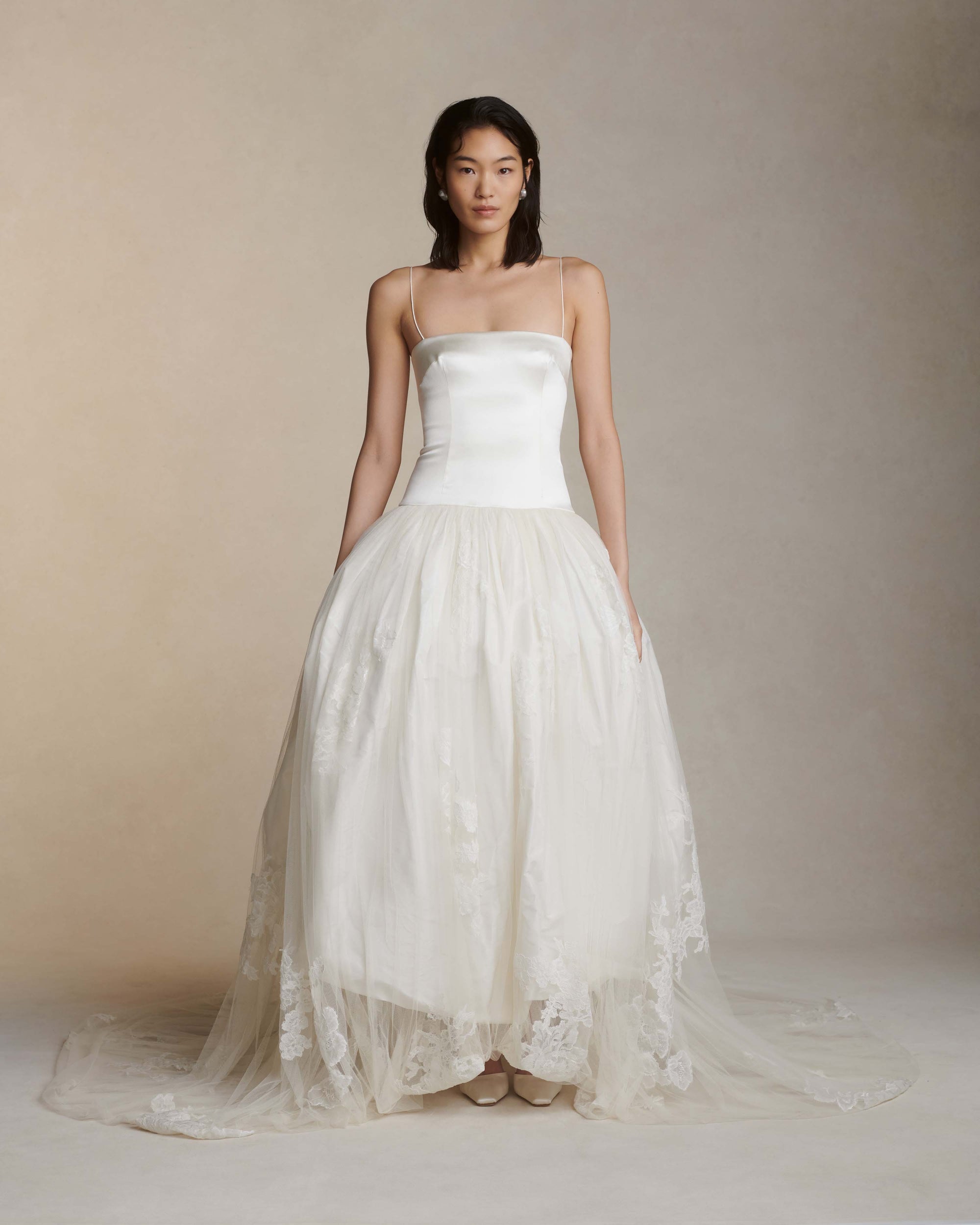 Fitted silk wool drop waist camisole bodice graduating into an airy silk taffeta bubble skirt. Soft tulle skirt overlay is adorned with hand cut chantilly and lace appliques. Straight neckline with spaghetti straps. Internal waist belt and center back zip closure.