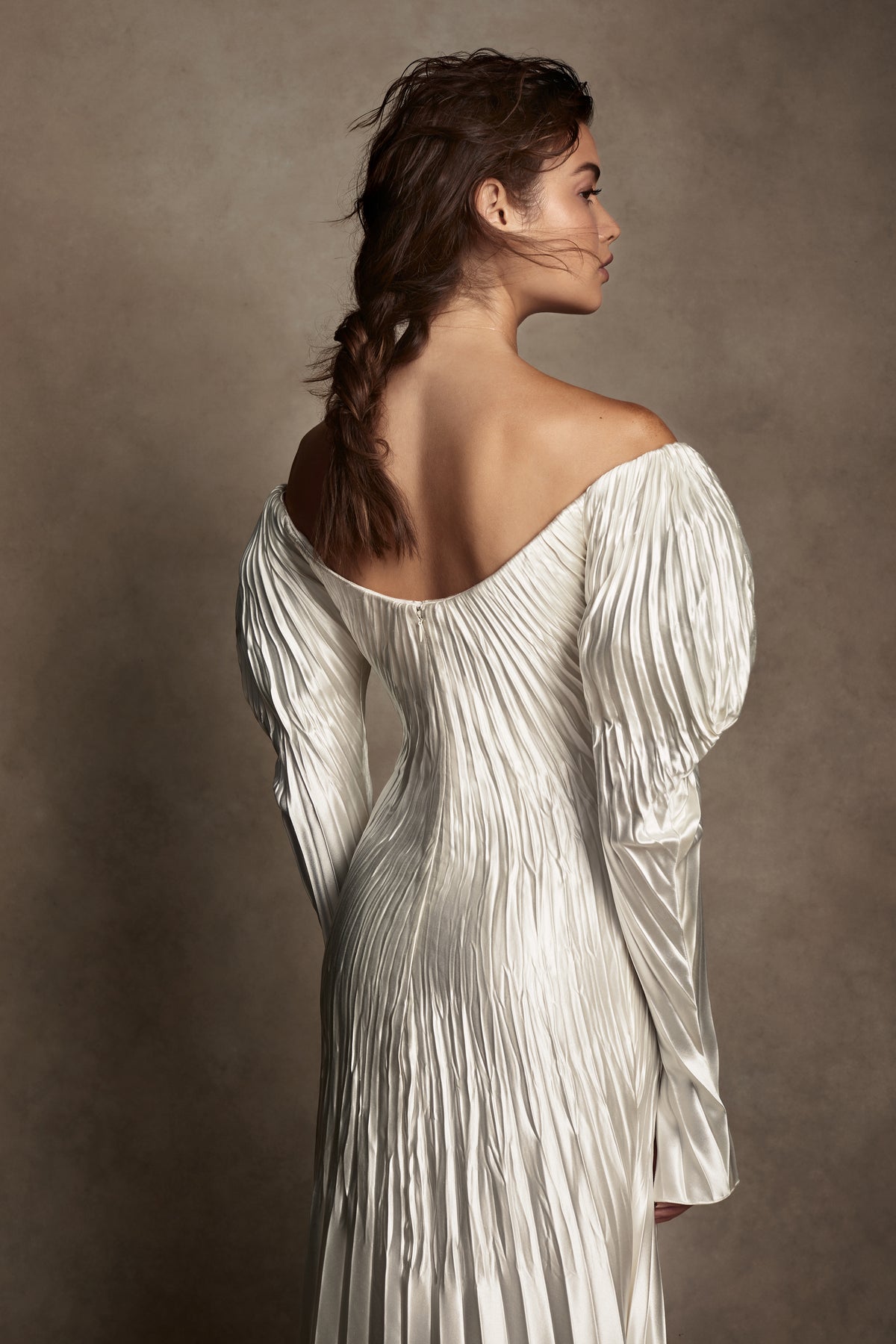 Pleated silk wool, exaggerated off the shoulder, floor length gown. Stiff neckline facing stay for structure and positioning of bodice framed by full length sleeves and 5 inch slit at inner wrist. Full internal power mesh corset with boning and internal and external center back zippers for security.Styled with Flaired Baroque Pearl Choker