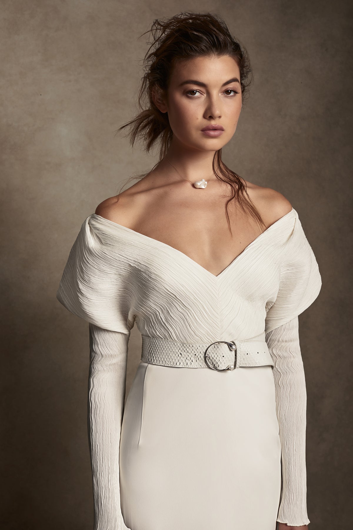 Off-shoulder gown with mini-pleated Georgette draped sleeves, and Grosgrain waist detail. Smooth faced Cady skirt, with circular train.Styled with Charlotte Skirt, Python Belt with Pearl Buckle and Flaired Baroque Pearl Drop Earrings.