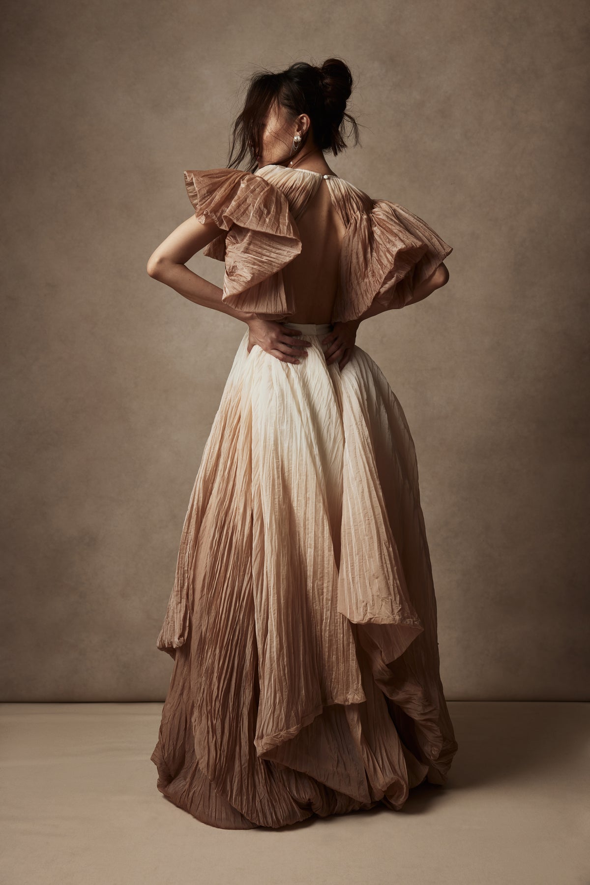 Dip dyed pleated paper organza gown with bubble hem and voluminous short ruffled sleeve. Center back zipper and external grosgrain belt atop soft tulle lined internal bustier. Crew neckline with button close at back of neck creating triangular shaped open back. Available in ivory upon request.