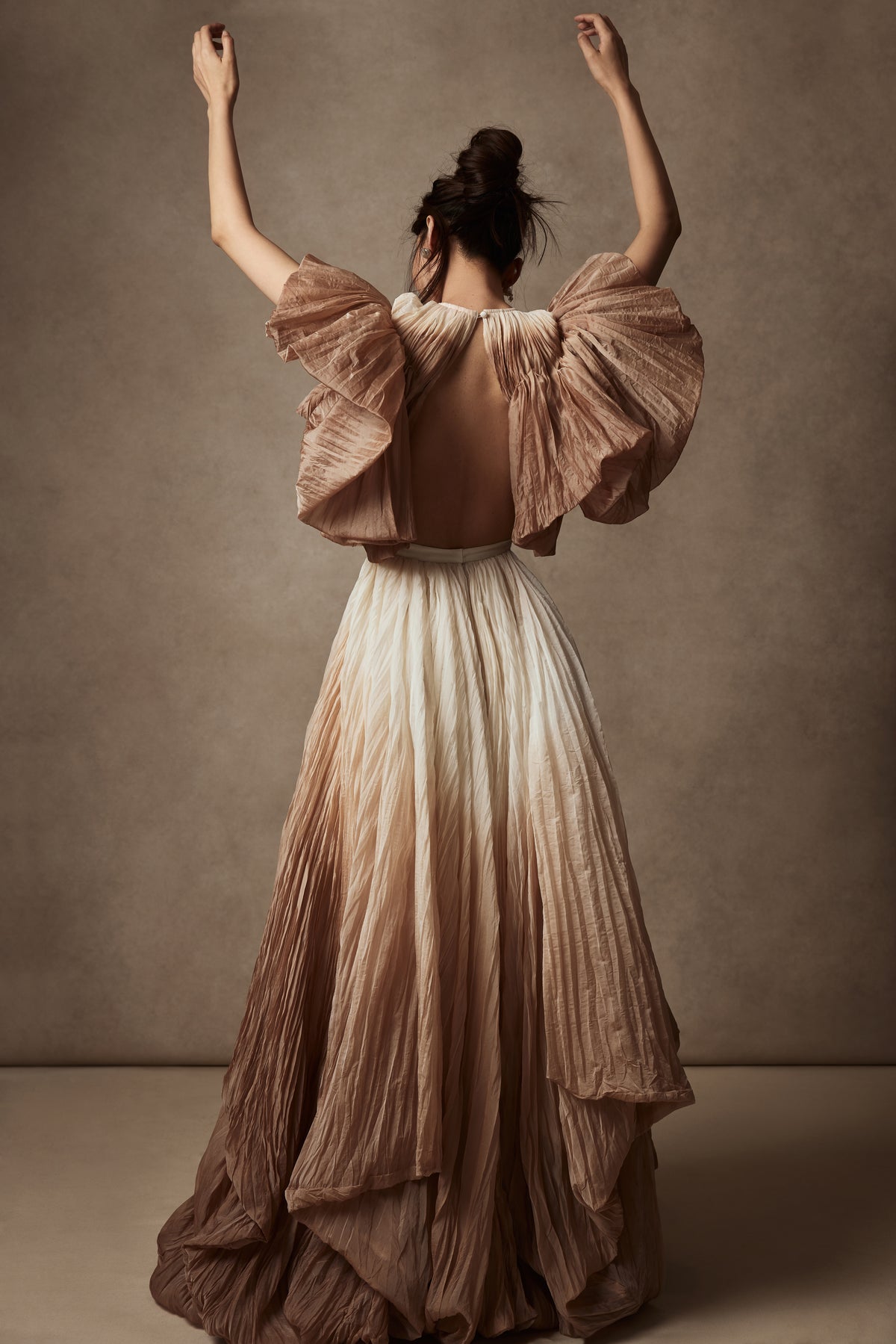 Dip dyed pleated paper organza gown with bubble hem and voluminous short ruffled sleeve. Center back zipper and external grosgrain belt atop soft tulle lined internal bustier. Crew neckline with button close at back of neck creating triangular shaped open back. Available in ivory upon request.
