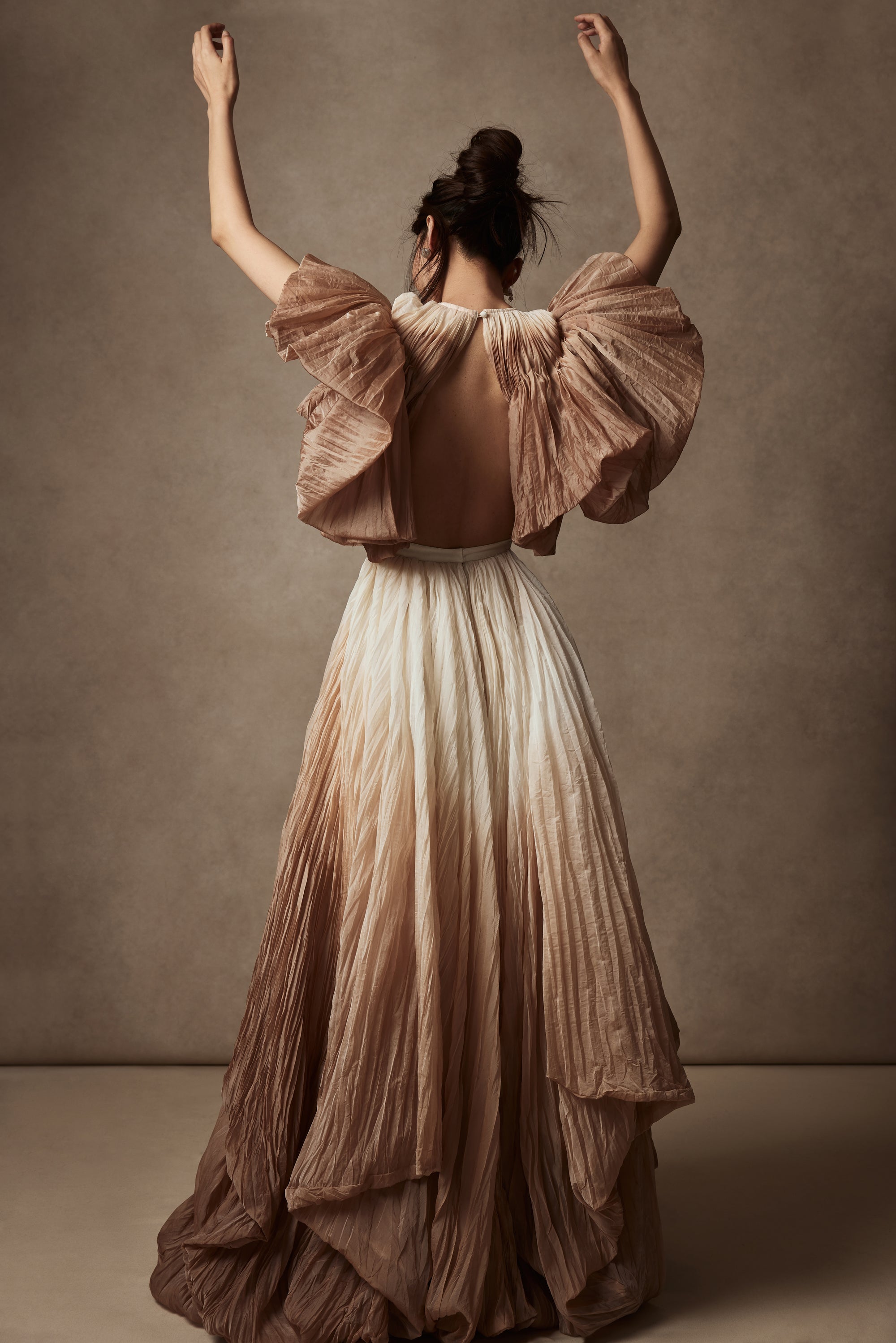 Dip dyed pleated paper organza gown with bubble hem and voluminous short ruffled sleeve. Center back zipper and external grosgrain belt atop soft tulle lined internal bustier. Crew neckline with button close at back of neck creating triangular shaped open back. Available in ivory upon request.