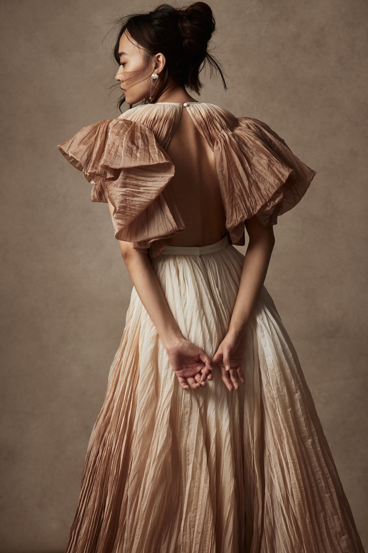Dip dyed pleated paper organza gown with bubble hem and voluminous short ruffled sleeve. Center back zipper and external grosgrain belt atop soft tulle lined internal bustier. Crew neckline with button close at back of neck creating triangular shaped open back. Available in ivory upon request.