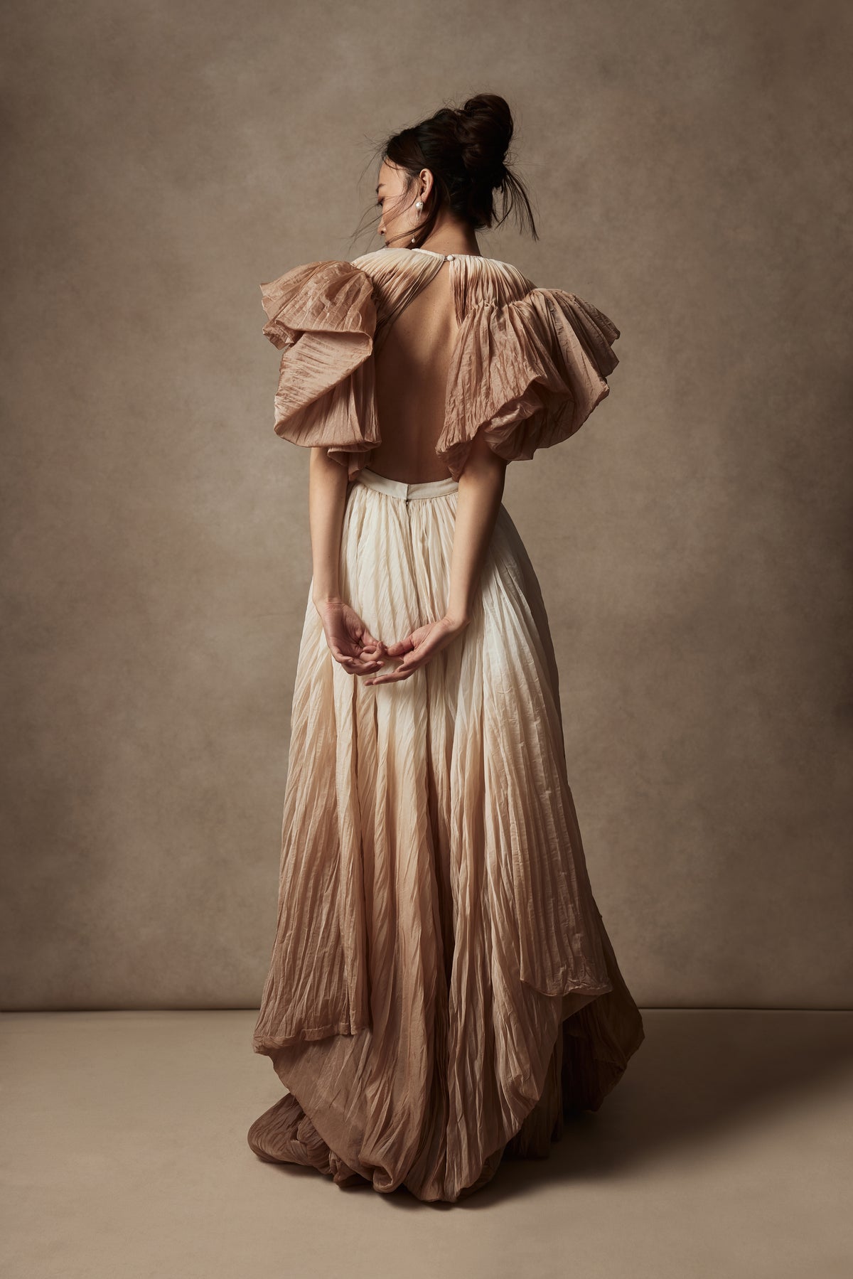 Dip dyed pleated paper organza gown with bubble hem and voluminous short ruffled sleeve. Center back zipper and external grosgrain belt atop soft tulle lined internal bustier. Crew neckline with button close at back of neck creating triangular shaped open back. Available in ivory upon request.