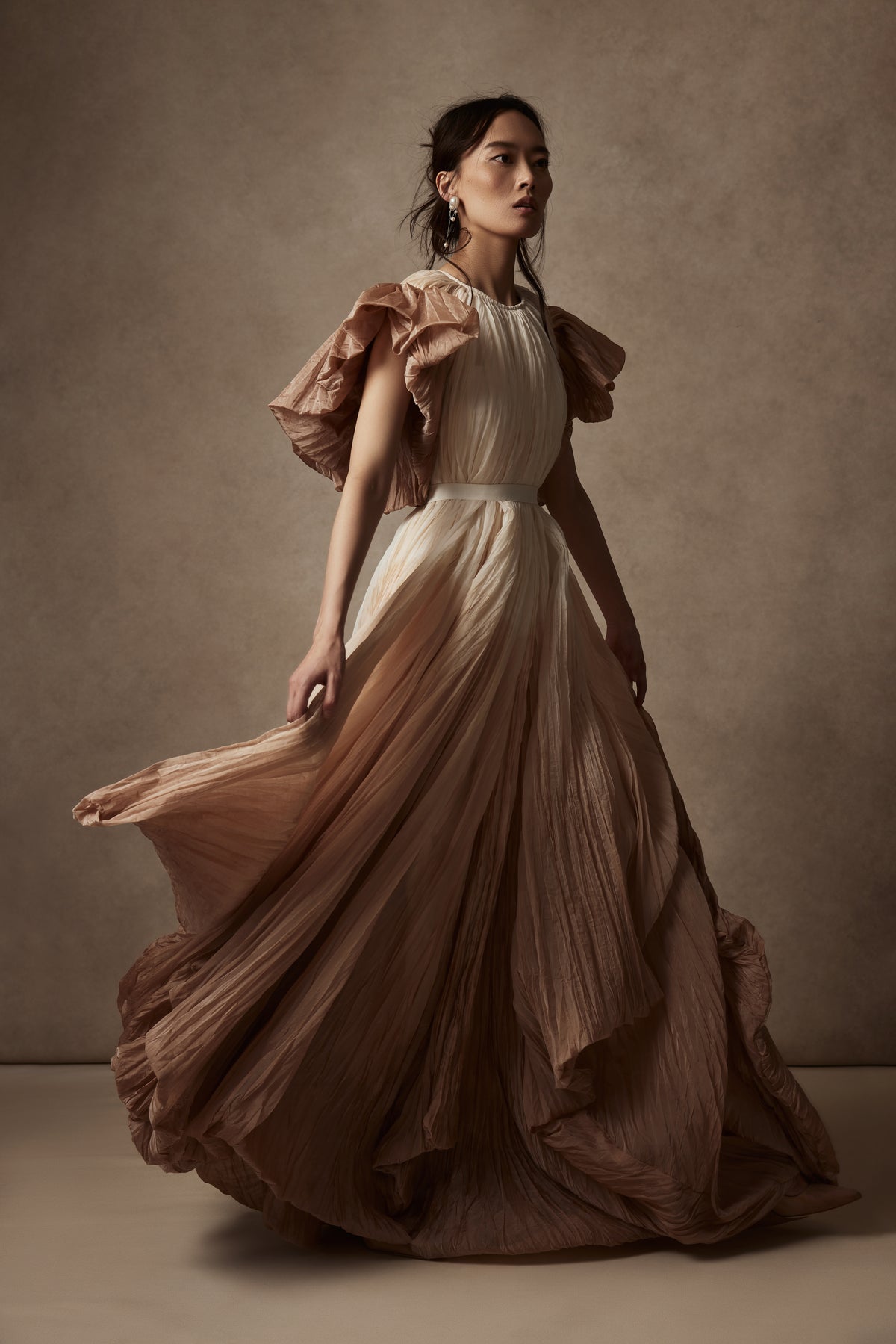 Dip dyed pleated paper organza gown with bubble hem and voluminous short ruffled sleeve. Center back zipper and external grosgrain belt atop soft tulle lined internal bustier. Crew neckline with button close at back of neck creating triangular shaped open back. Available in ivory upon request.