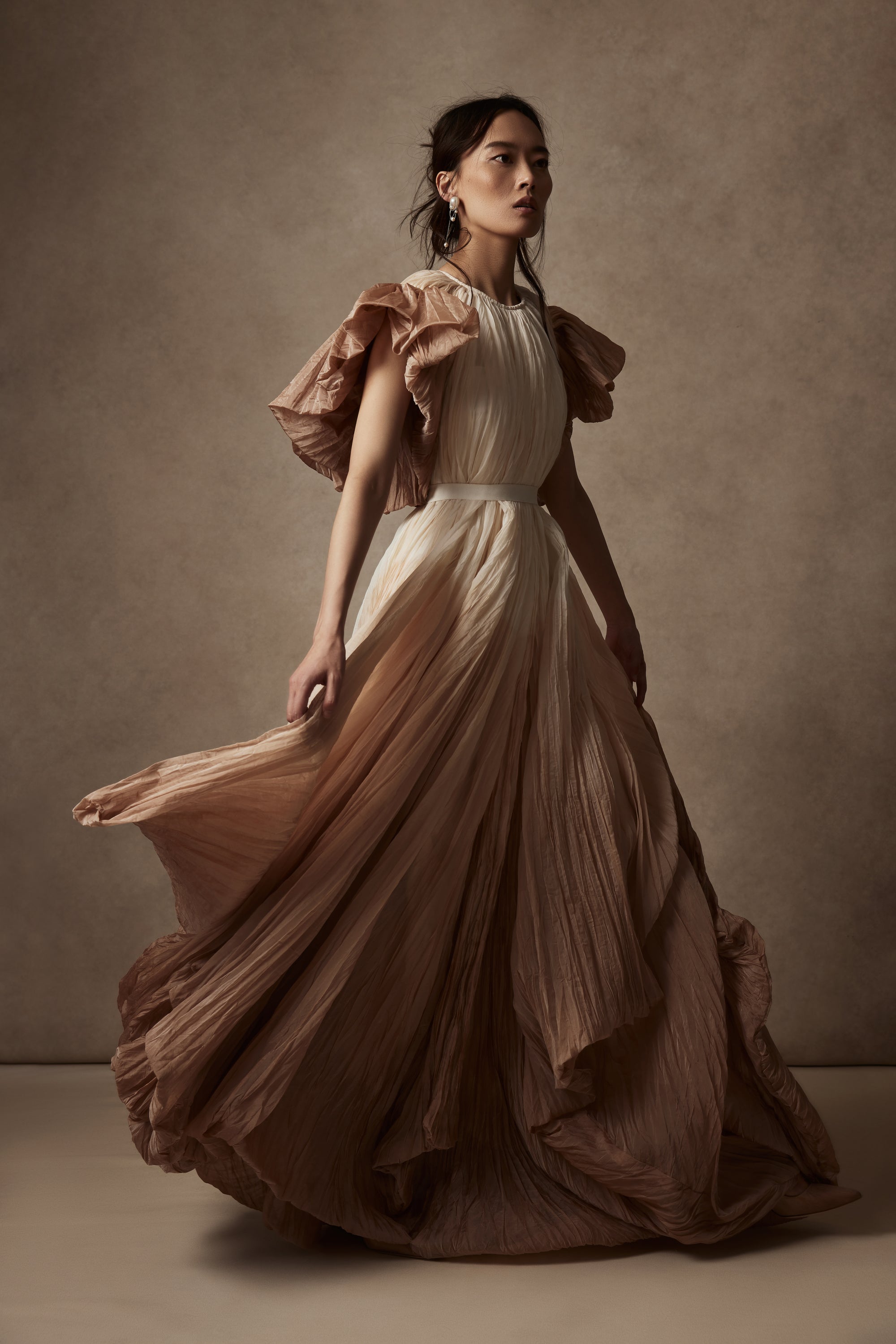Dip dyed pleated paper organza gown with bubble hem and voluminous short ruffled sleeve. Center back zipper and external grosgrain belt atop soft tulle lined internal bustier. Crew neckline with button close at back of neck creating triangular shaped open back. Available in ivory upon request.