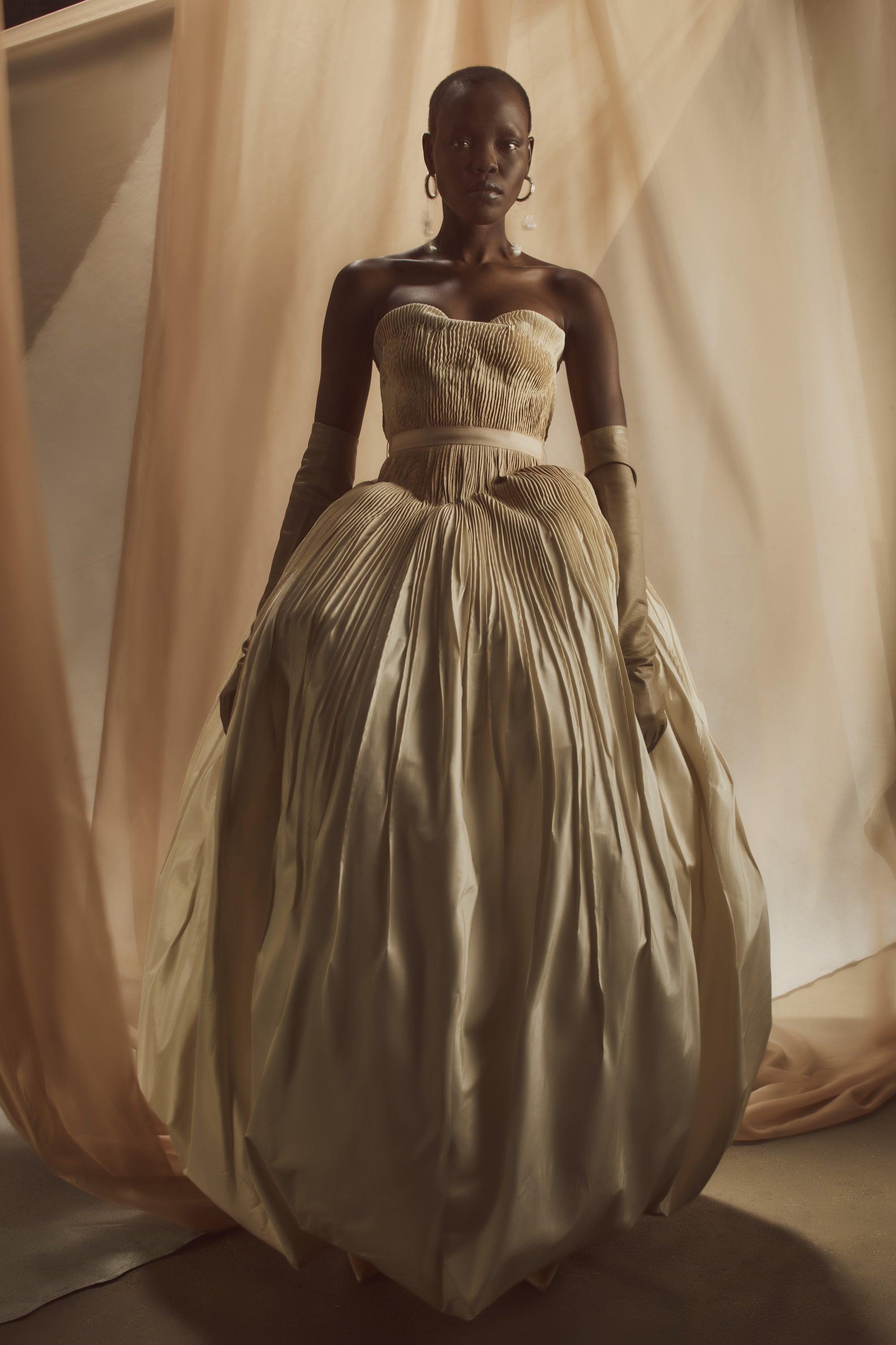Hand tucked silk taffeta gown with dipped neckline. Micro tucked drop waist bodice with grosgrain waist tie releases into a dramatic skirt with bubbled hem. Hand-dyed ombre bodice fades from under bust and into skirt. Soft internal cups, boning, internal waist belt, invisible center back zip. Available in Ivory $10,990.