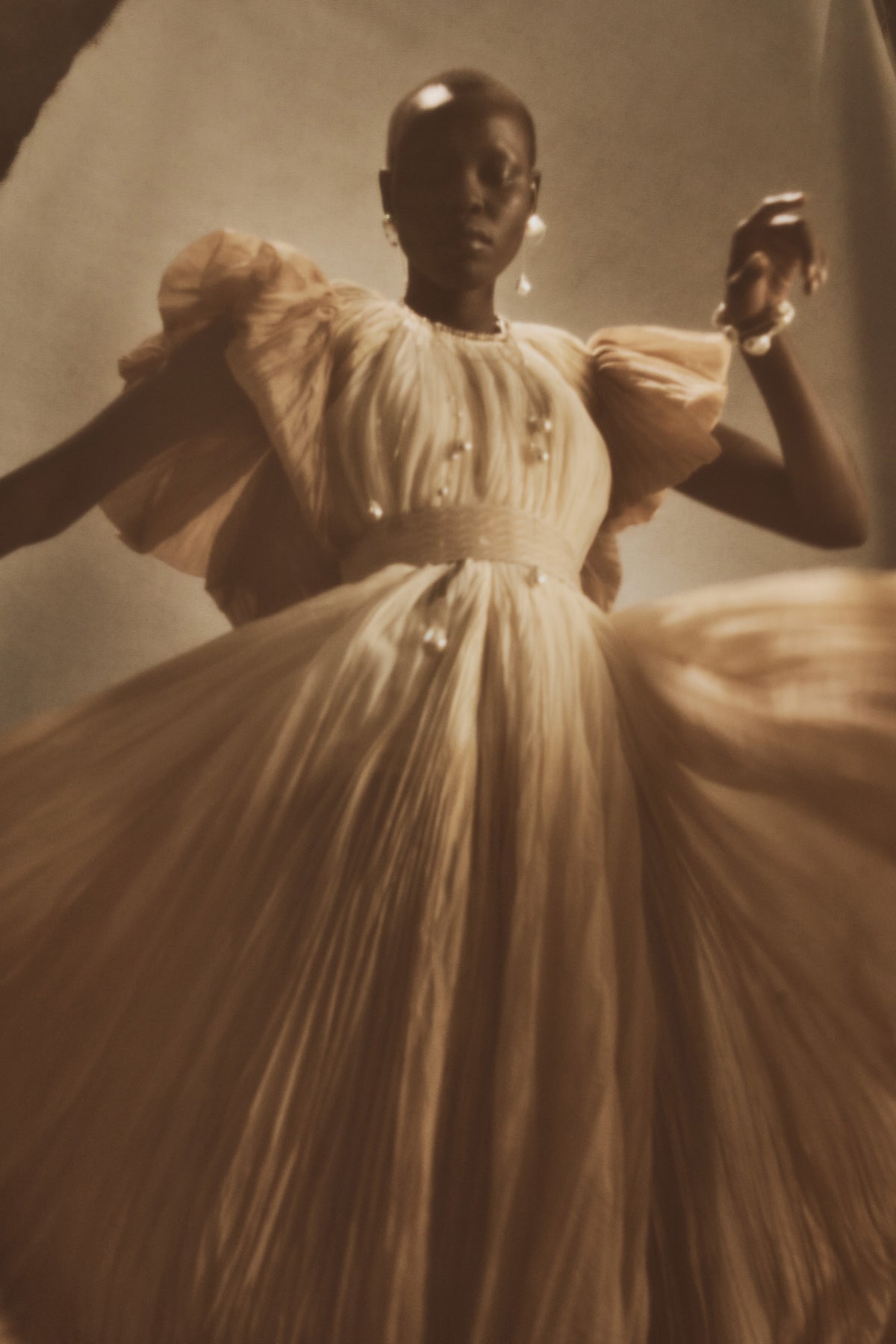Dip dyed pleated paper organza gown with bubble hem and voluminous short ruffled sleeve. Center back zipper and external grosgrain belt atop soft tulle lined internal bustier. Crew neckline with button close at back of neck creating triangular shaped open back. Available in ivory upon request.