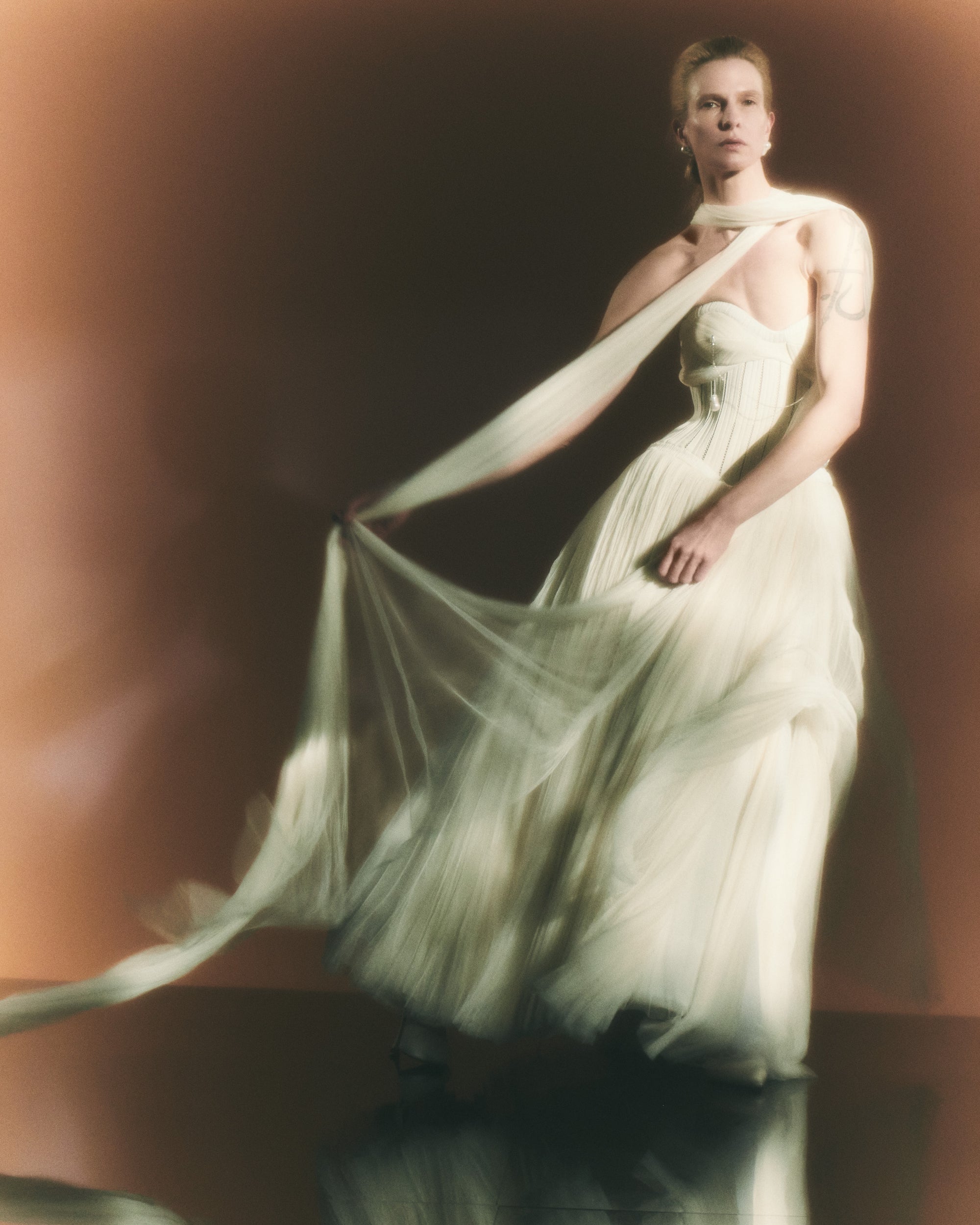 Tulle and twill corseted tea length ball gown. Lace and piped cotton twill bodice with full hook and eye back closure. Exaggerated soft tulle, pleated panels at bust to drape over the body. Sunburst pleated, hand crinkled tulle skirt upon silk organza base. Crinoline for structure and center back zip to close.