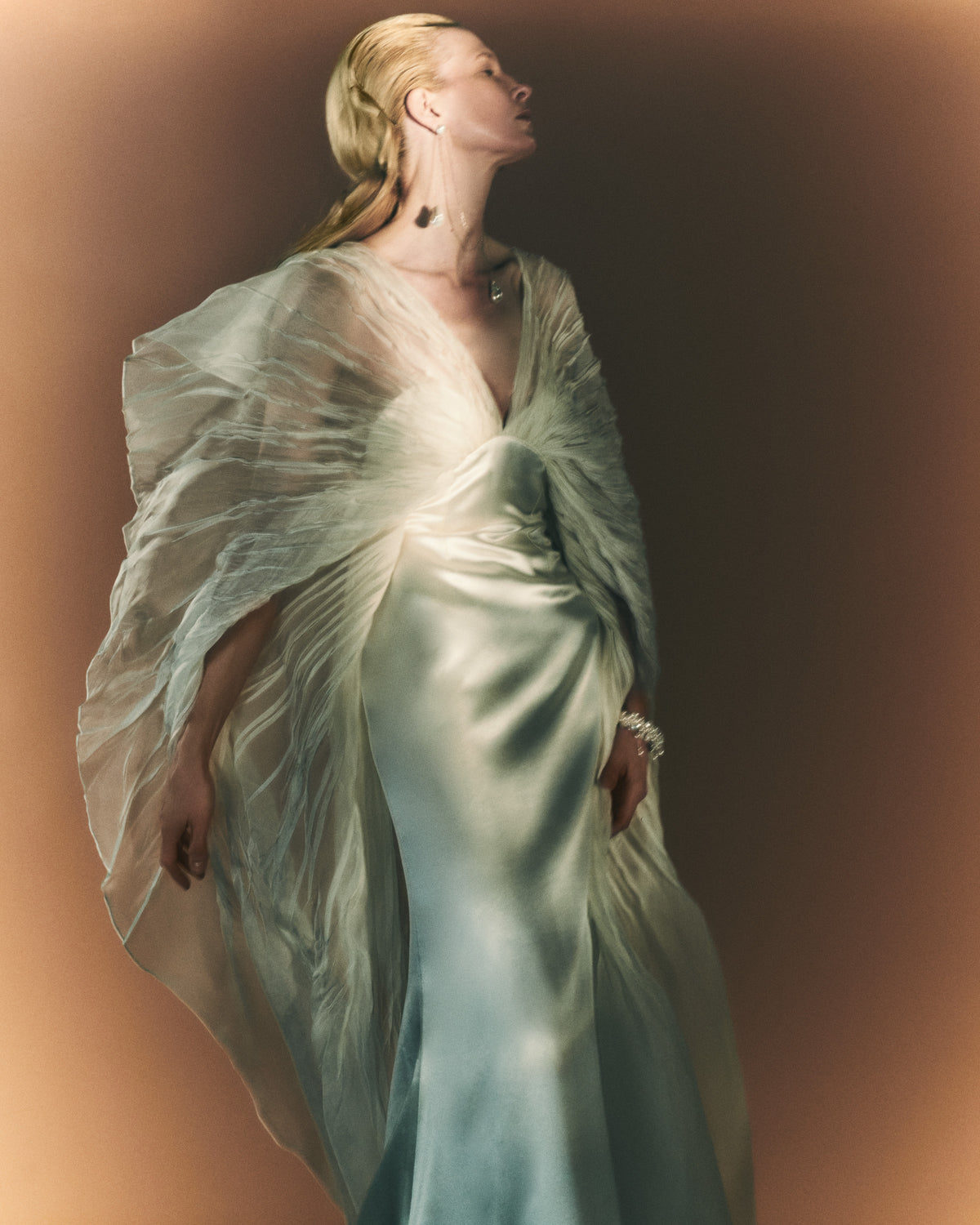Silk wool and pin-tucked organza cape gown. Billowing, hand pleated organza sleeve releasing from center front of camisole slip gown to spaghetti strap back. Organza pin-tuck bursts along low v-back into extended train. Soft body construction and center back close.