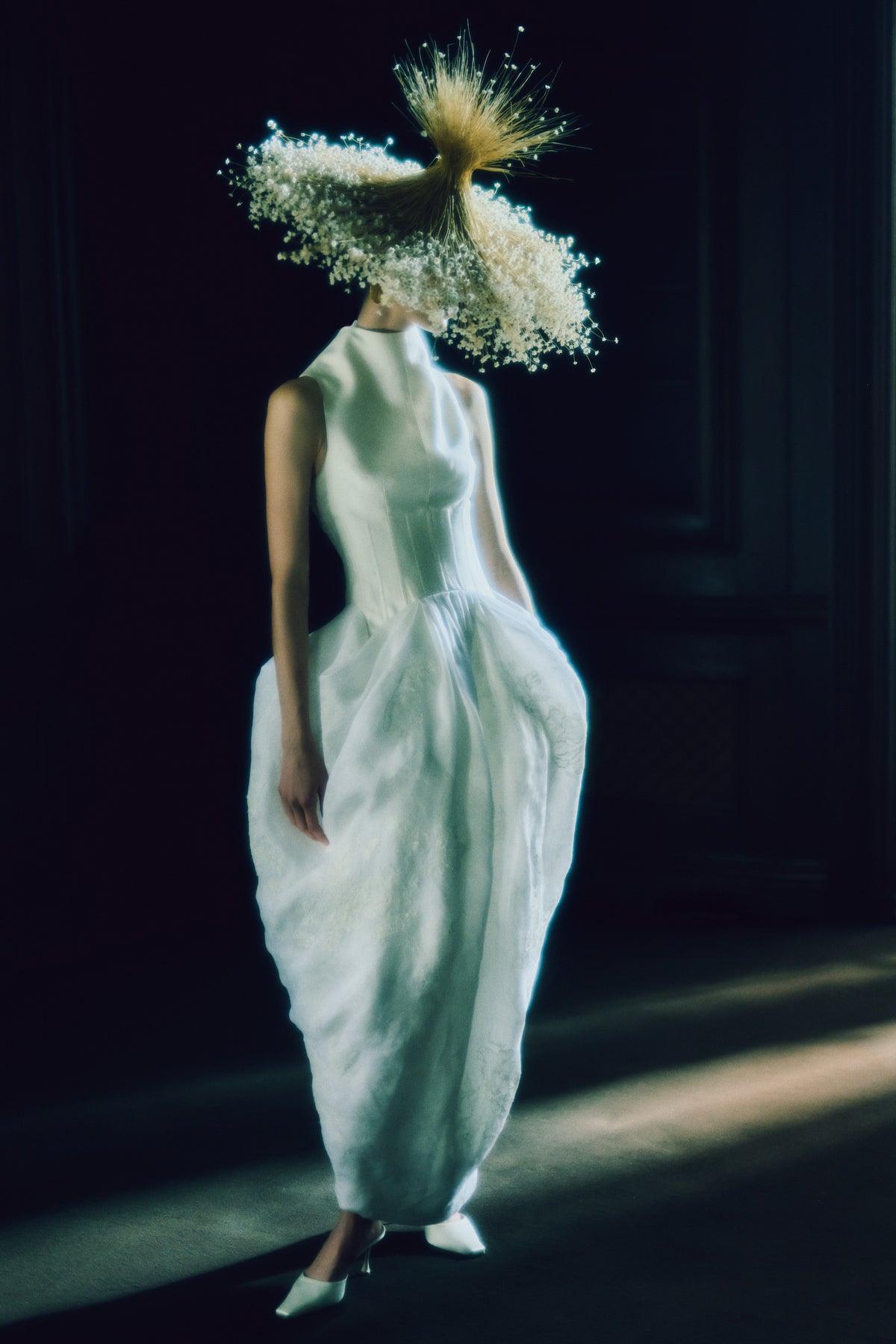 Silk wool twill and linen organza tea length gown. Structured boned bodice extends into dramatic sloped high neck that floats away from the body. Pleated and draped skirt is adorned with hand cut chantilly and corded lace appliques. Center back zip closure.