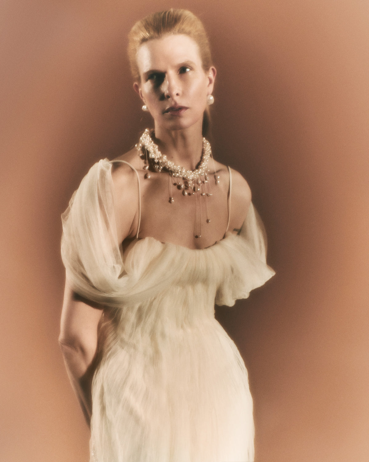 Pleated tulle swagged gown. Off the shoulder soft drapes releasing from center neckline to spaghetti strap back. Sunburst pleated, hand crinkled soft tulle through body and extending down center back for shape and movement. Soft internal bustier with side boning. Low center back zip, hook and eye closure.