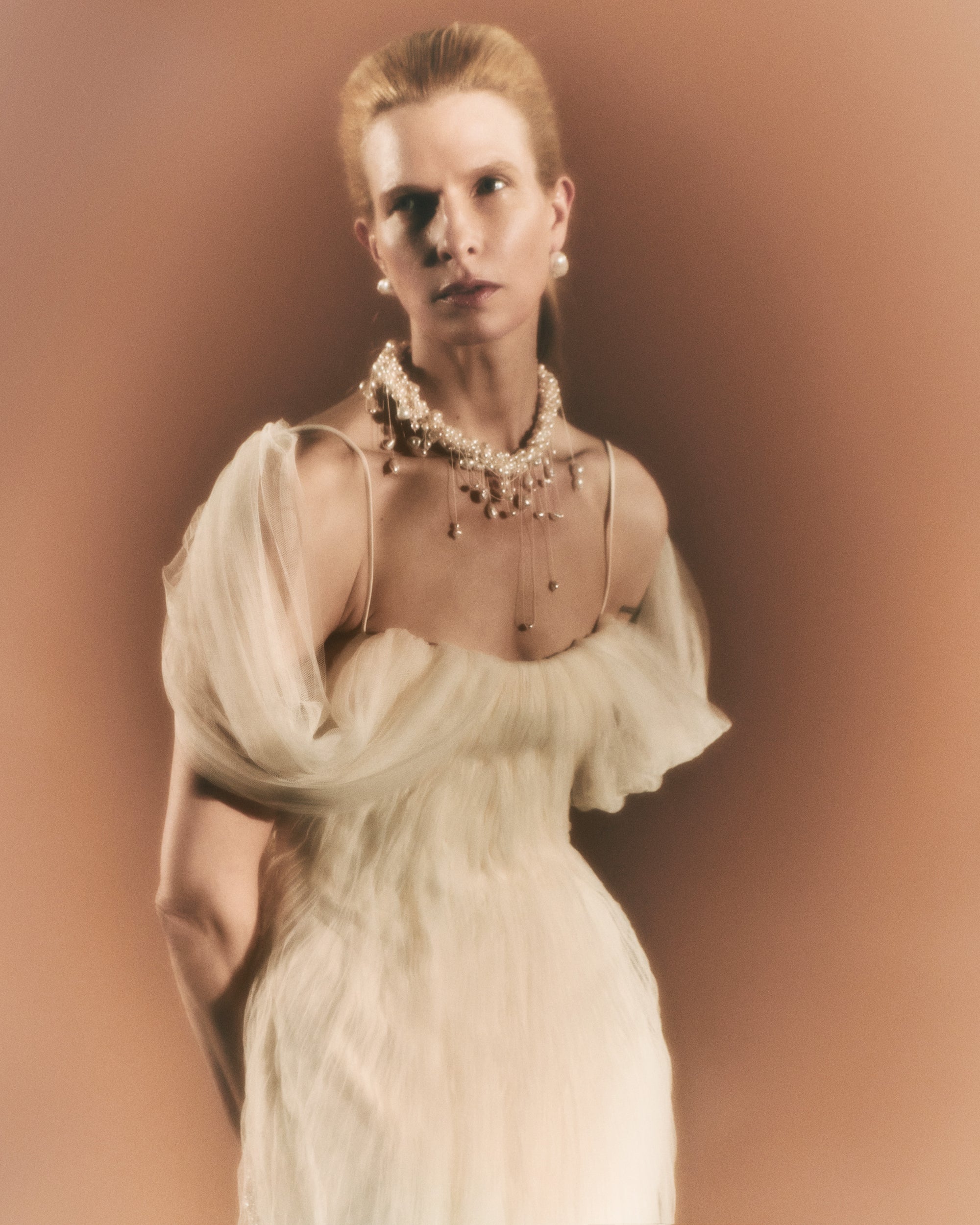 Pleated tulle swagged gown. Off the shoulder soft drapes releasing from center neckline to spaghetti strap back. Sunburst pleated, hand crinkled soft tulle through body and extending down center back for shape and movement. Soft internal bustier with side boning. Low center back zip, hook and eye closure.