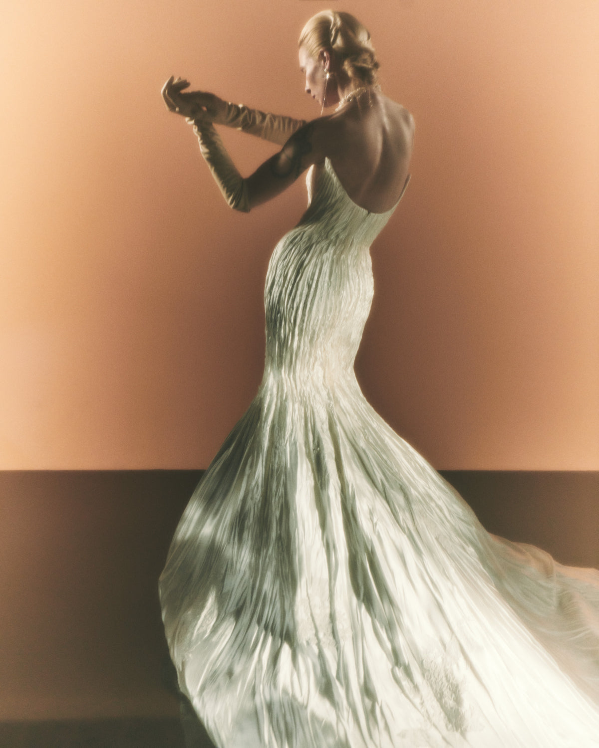 Silk wool hand crinkled gown fluted gown. Carved and sculpted strapless neckline. Hand appliquéd chantilly and corded lace motifs through body. Bubbled ankle grazing hem at front graduating into dramatic bubbled train. Soft internal corset with boning and center back zip closure.