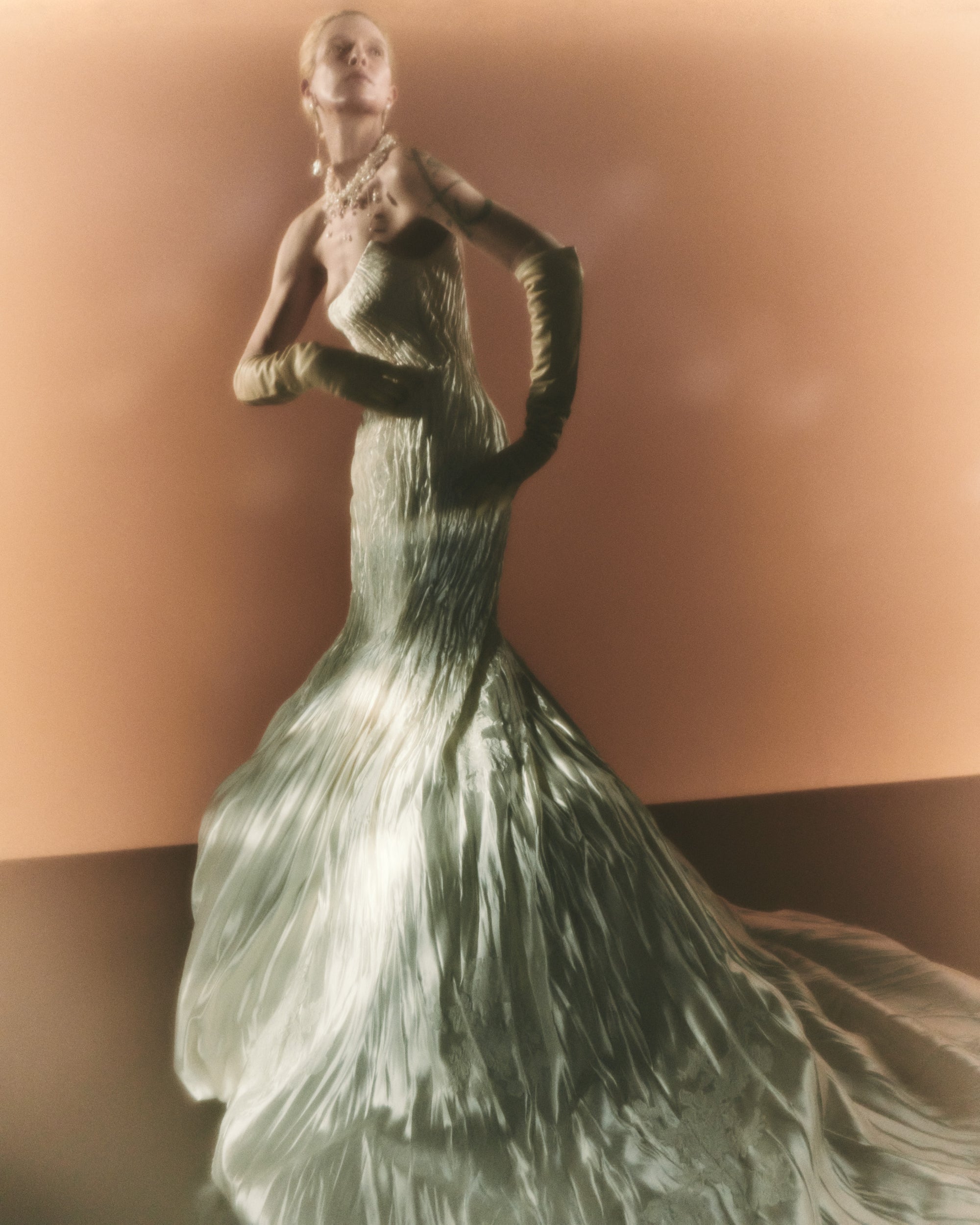 Silk wool hand crinkled gown fluted gown. Carved and sculpted strapless neckline. Hand appliquéd chantilly and corded lace motifs through body. Bubbled ankle grazing hem at front graduating into dramatic bubbled train. Soft internal corset with boning and center back zip closure.