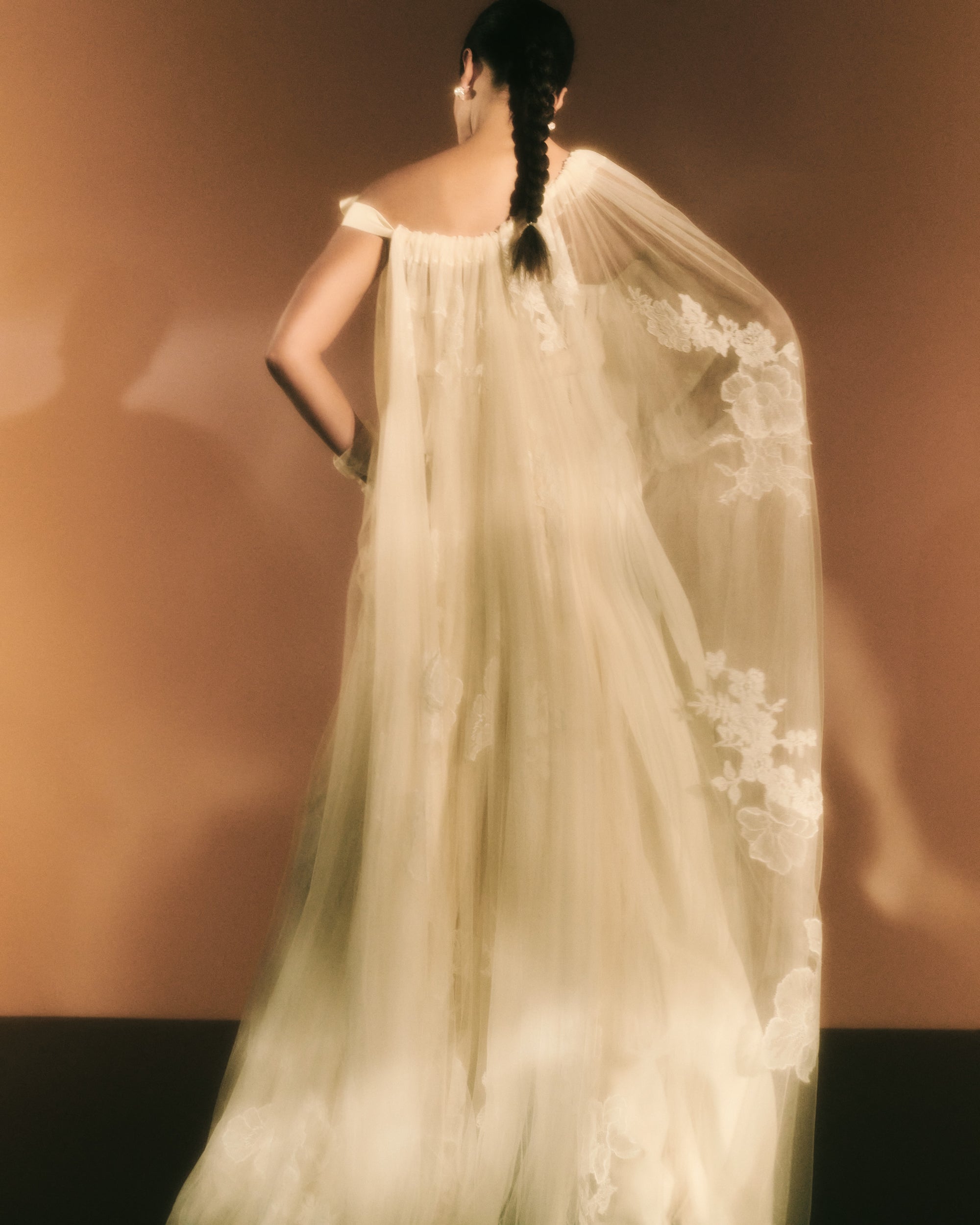 Soft tulle cape decorated with hand cut Chantilly and corded lace appliqués throughout Undulating hem measures 85” at longest point. Grosgrain ribbon tie.